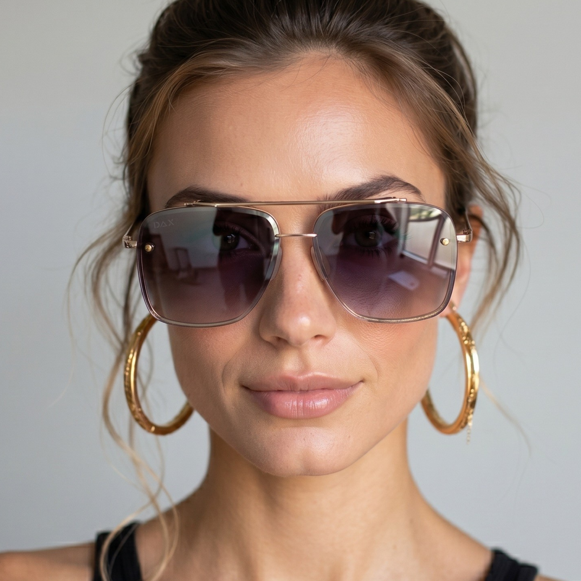 Woman wearing large hoop earrings and sunglasses against a neutral background
