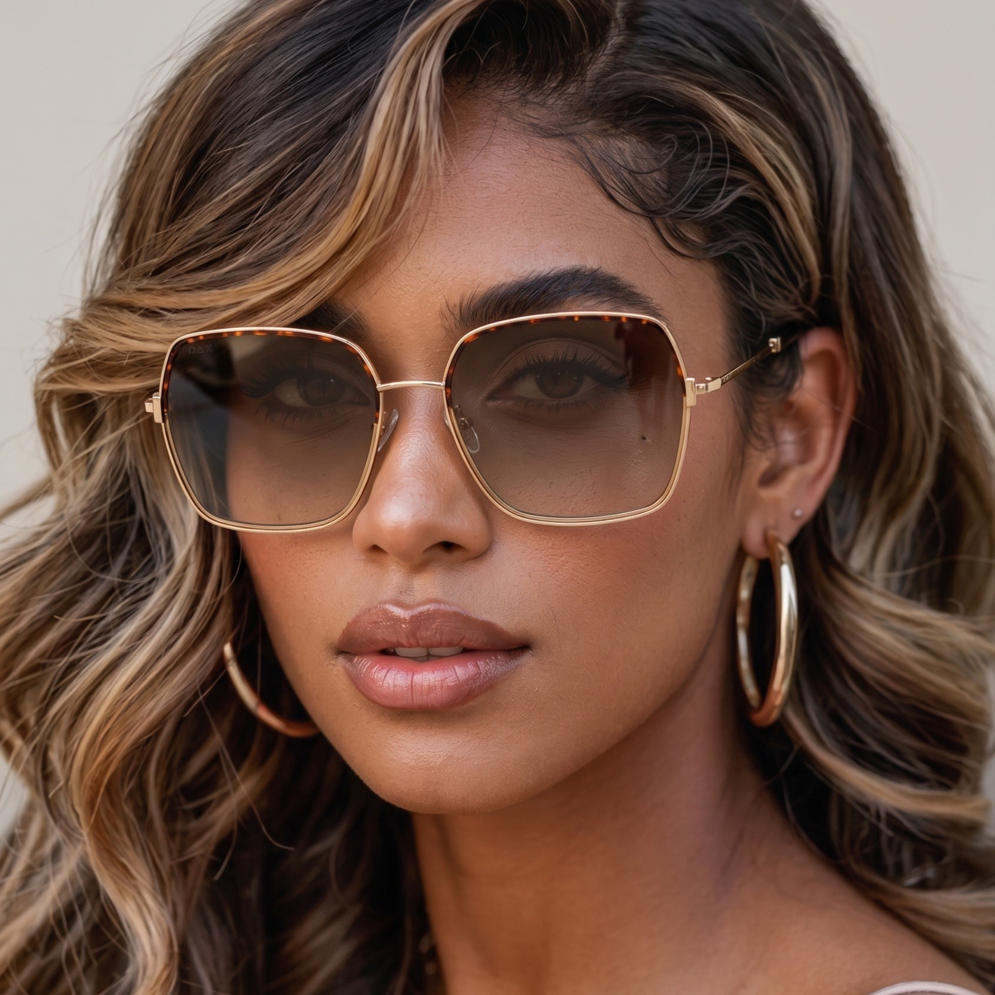 Woman wearing large sunglasses and hoop earrings with a neutral background