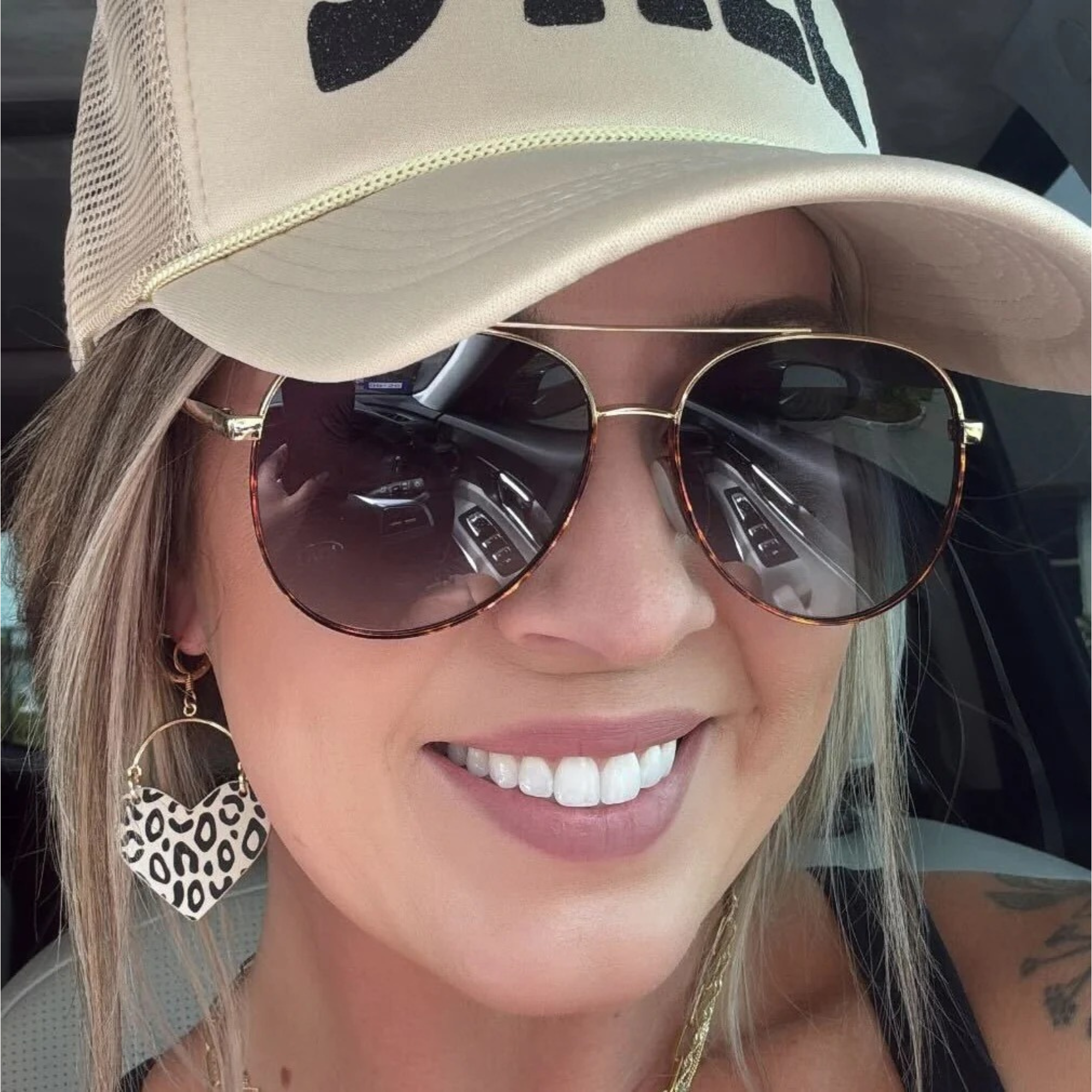 Woman wearing a beige cap and sunglasses with leopard print earrings.
