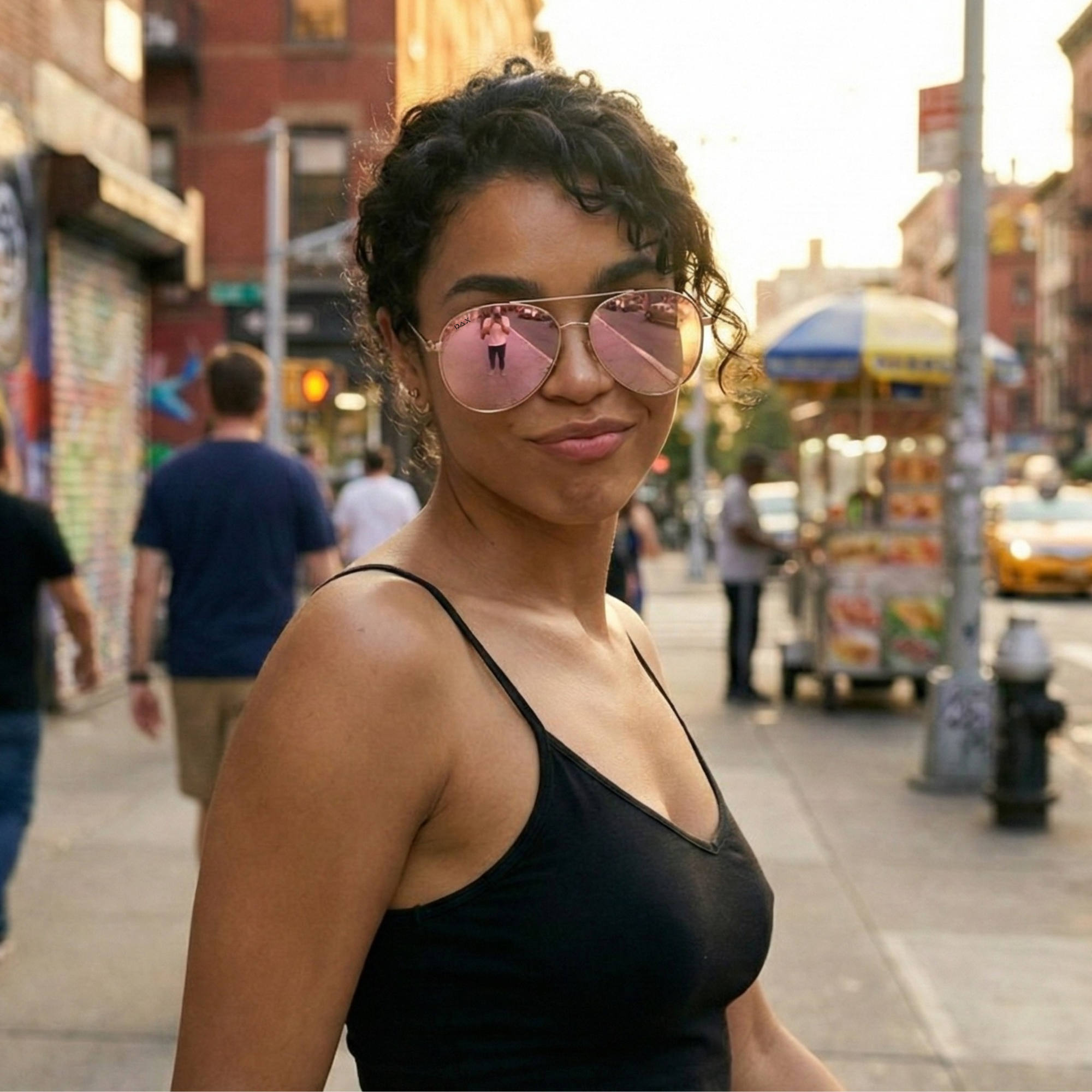 Woman wearing pink sunglasses and a black tank top on a city street.