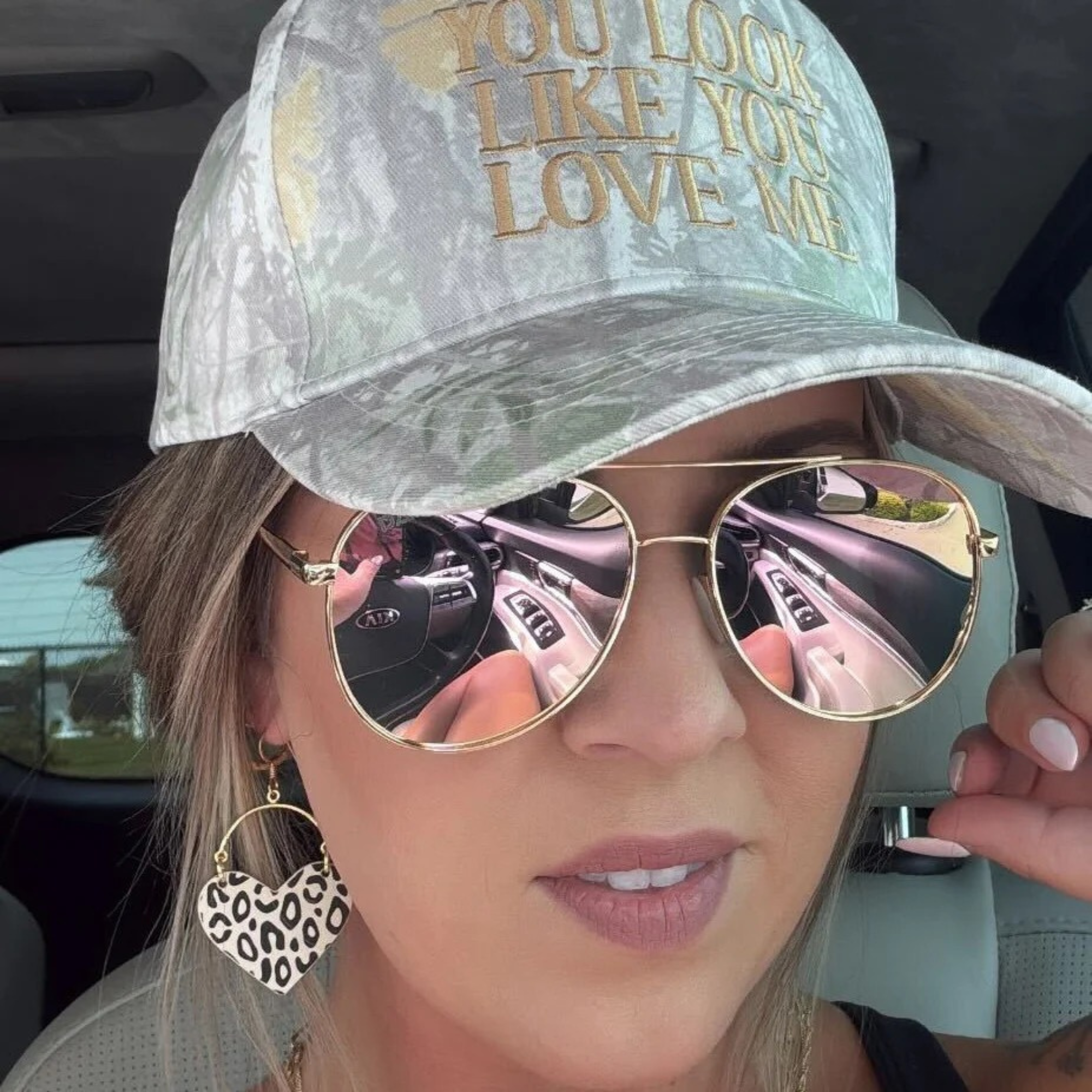 Person wearing a cap with text and sunglasses, sitting inside a vehicle.