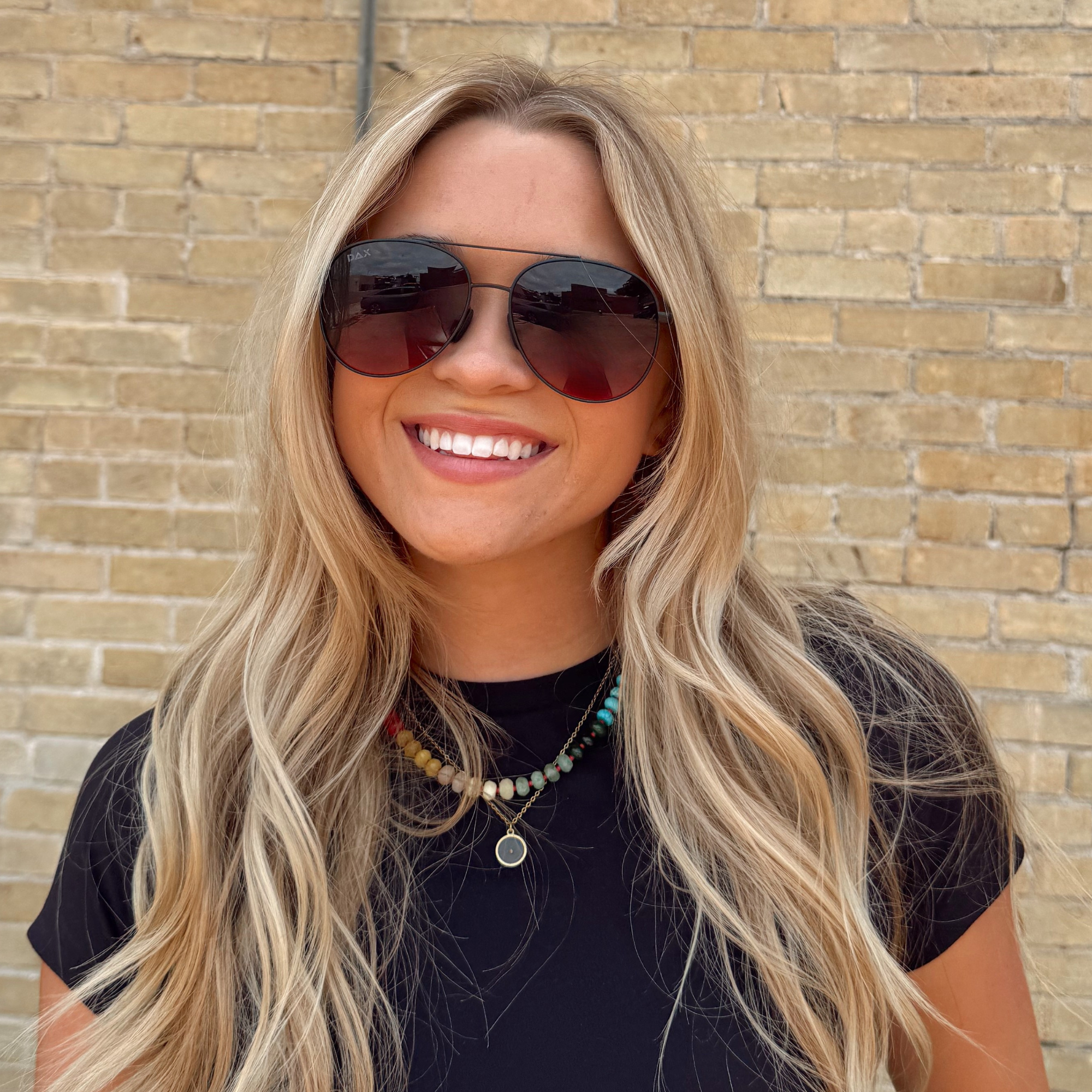 Woman wearing sunglasses and a black top against a brick wall