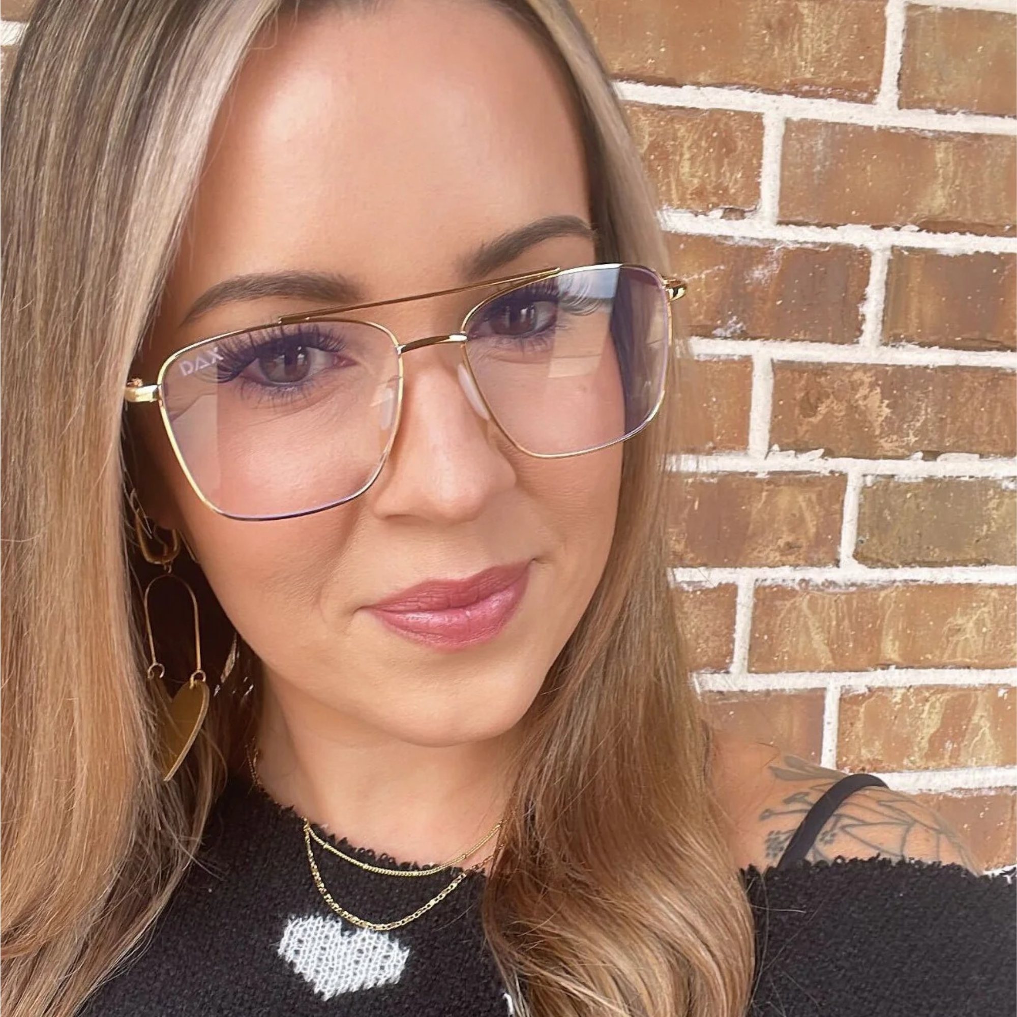Woman wearing gold-framed glasses with a brick wall background