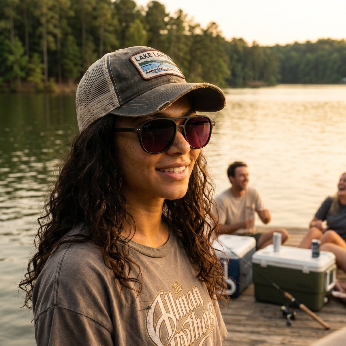 Woman wearing sunglasses and a cap by a lake with friends in the background