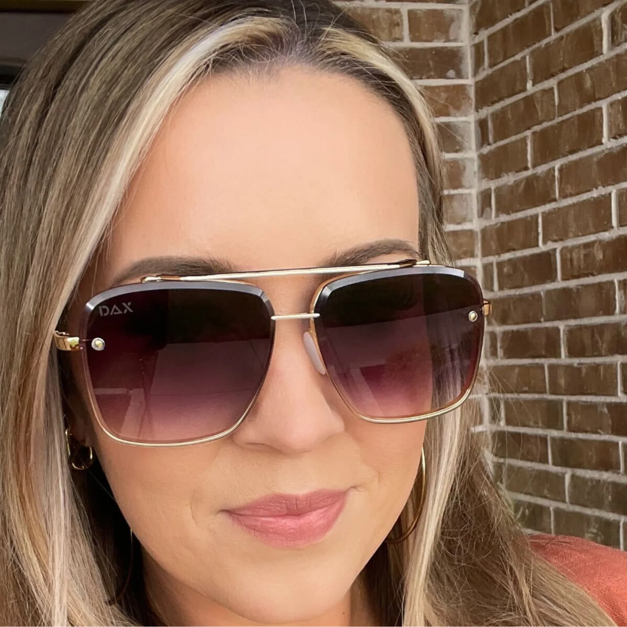 Woman wearing gold-framed sunglasses with a brick wall background