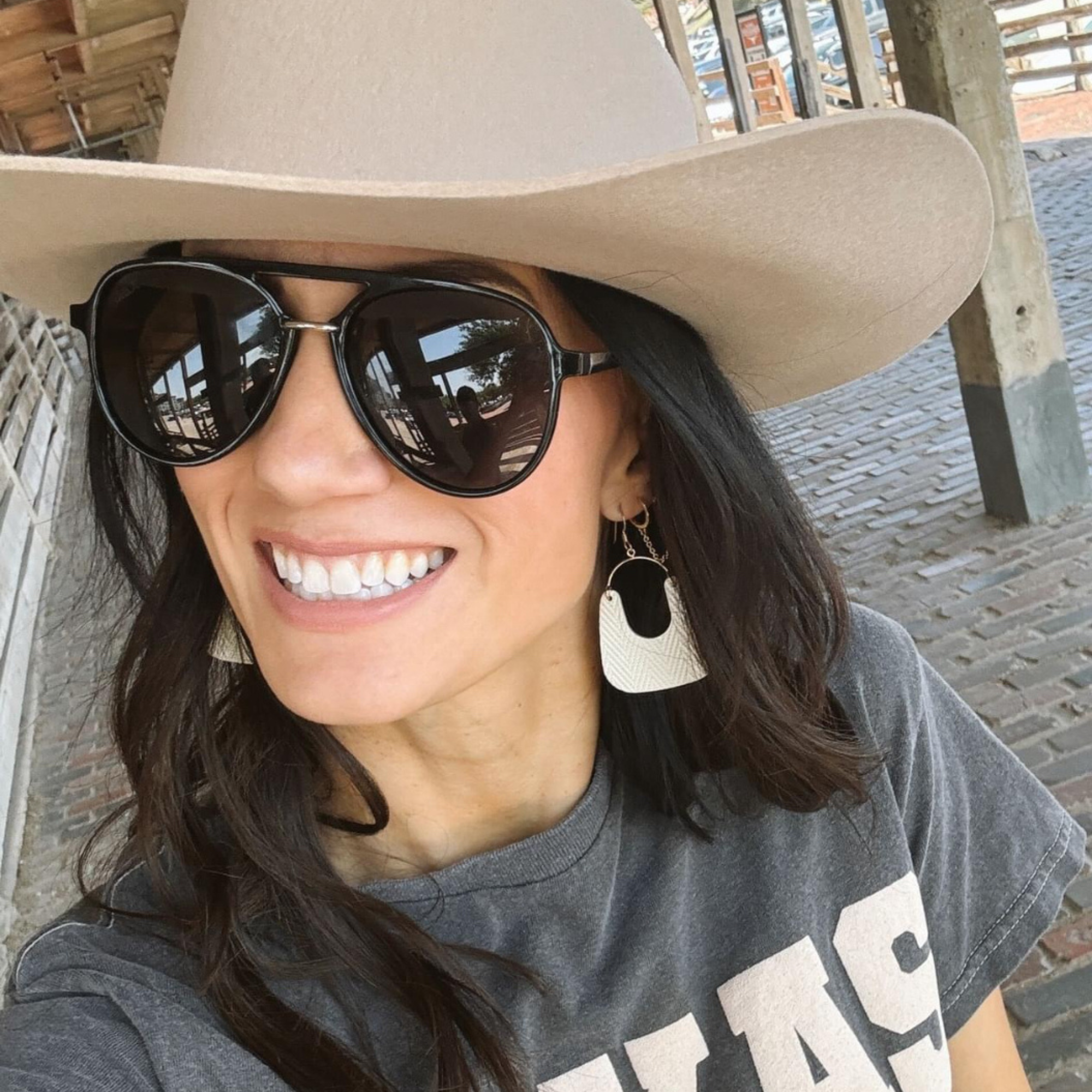Woman wearing a wide-brimmed hat and sunglasses, smiling outdoors.