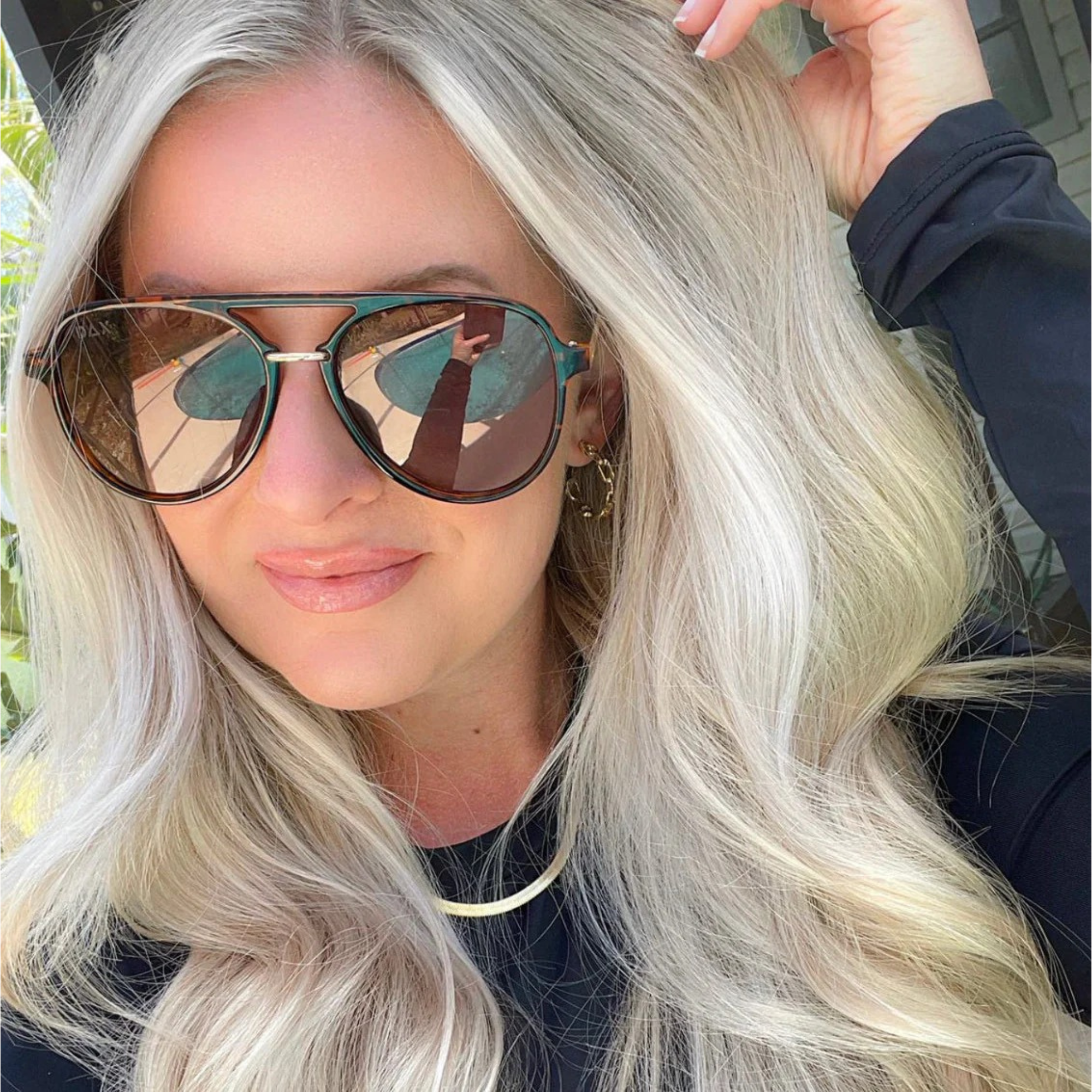 Woman with long blonde hair wearing reflective sunglasses outdoors