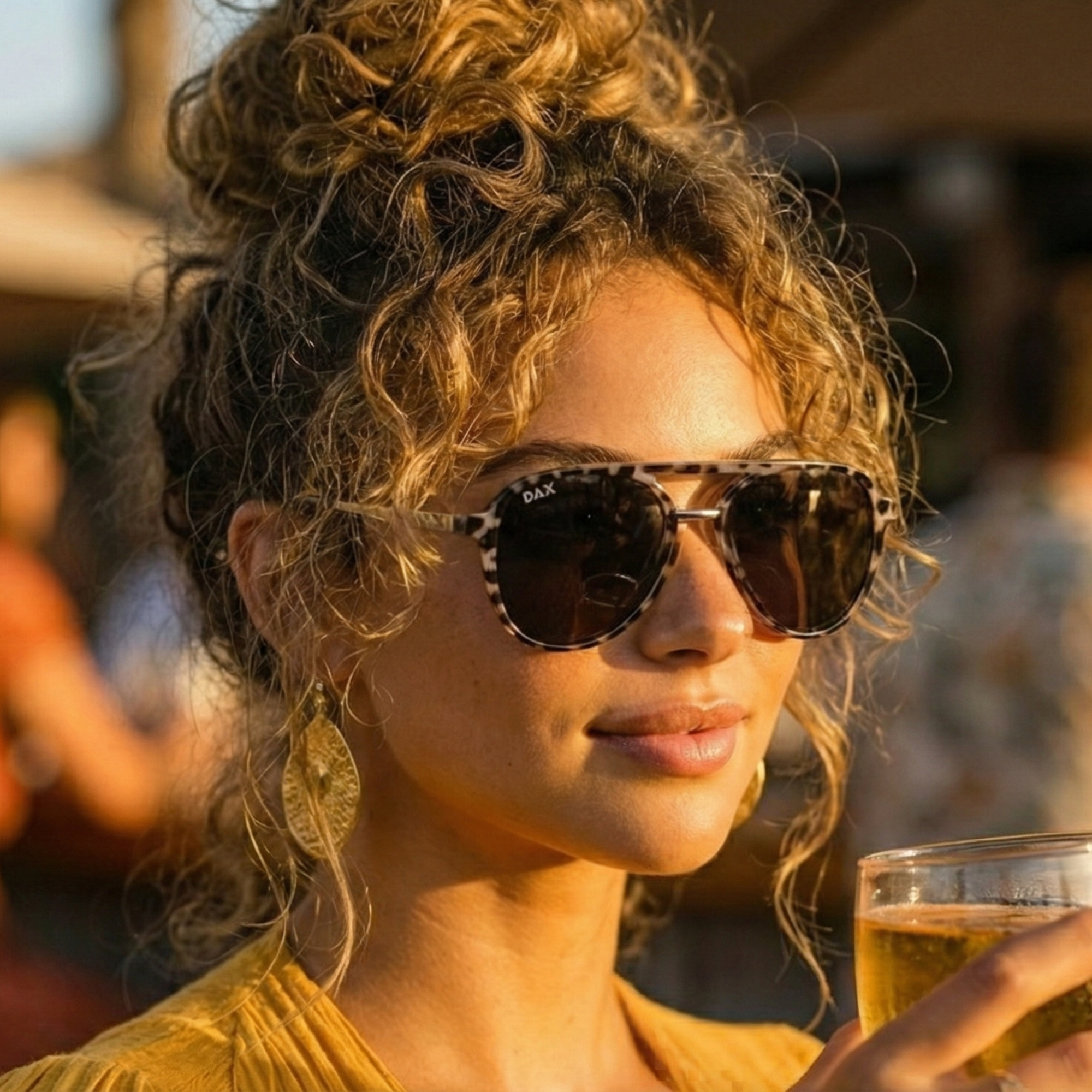 Woman wearing sunglasses and holding a drink with a blurred background