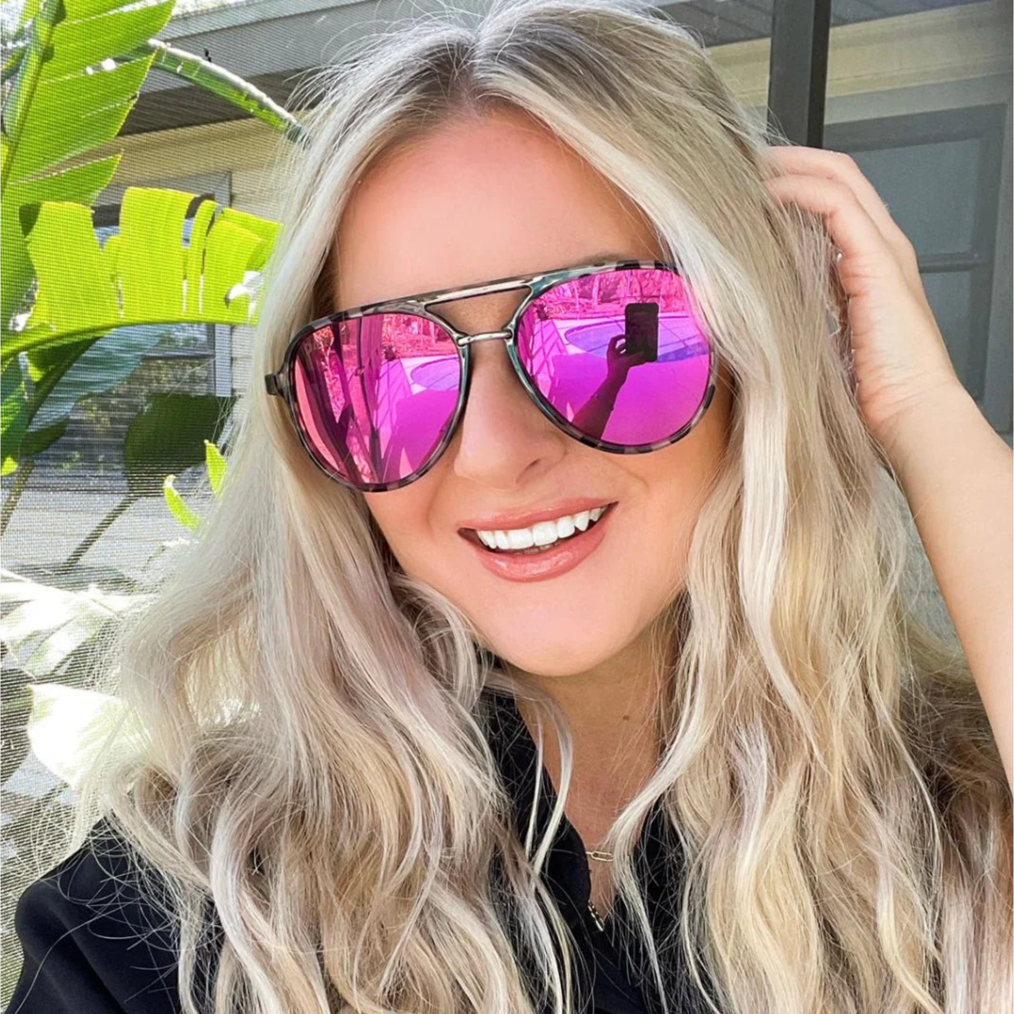 Woman wearing pink reflective sunglasses with a blurred outdoor background
