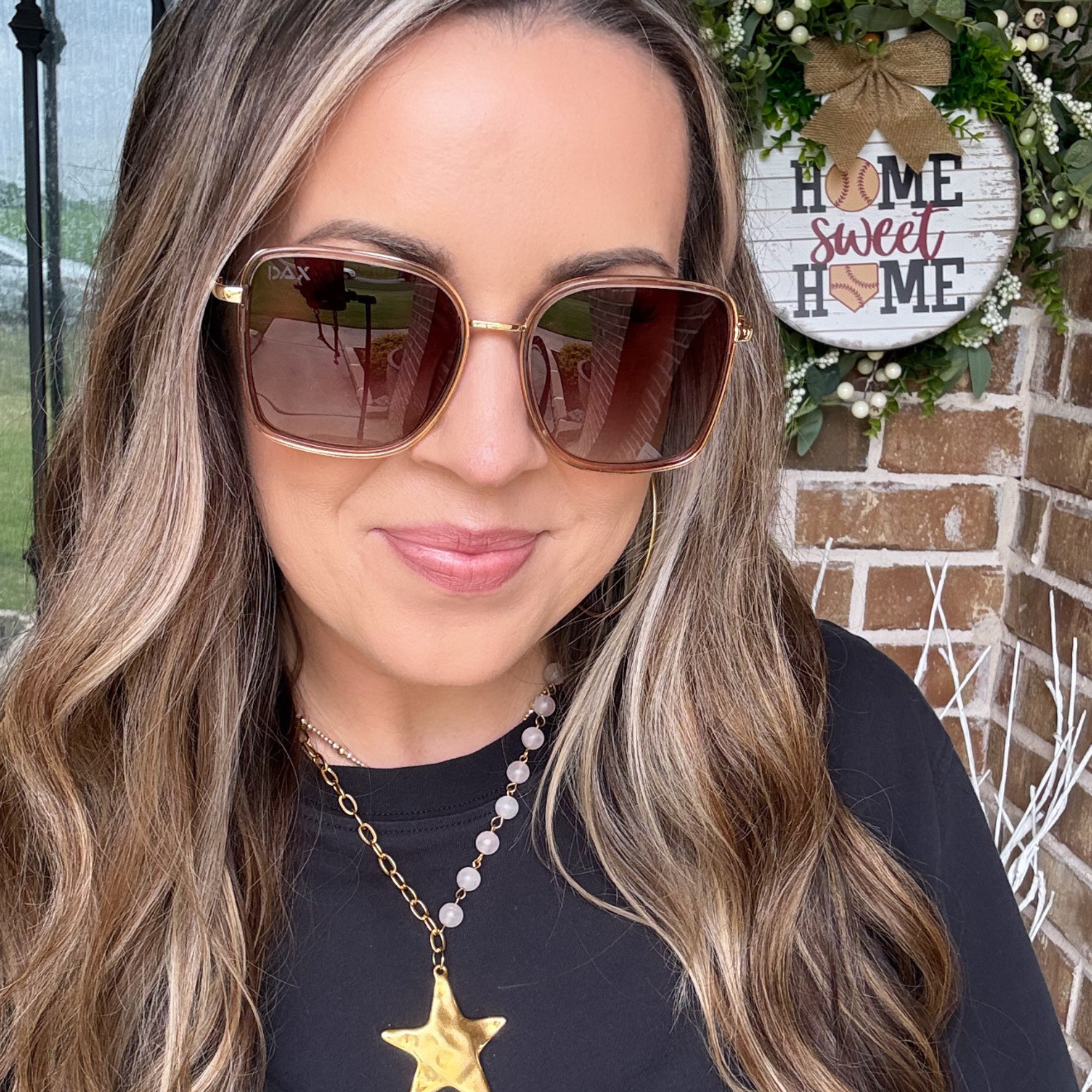 Woman wearing sunglasses with a 'Home Sweet Home' sign in the background