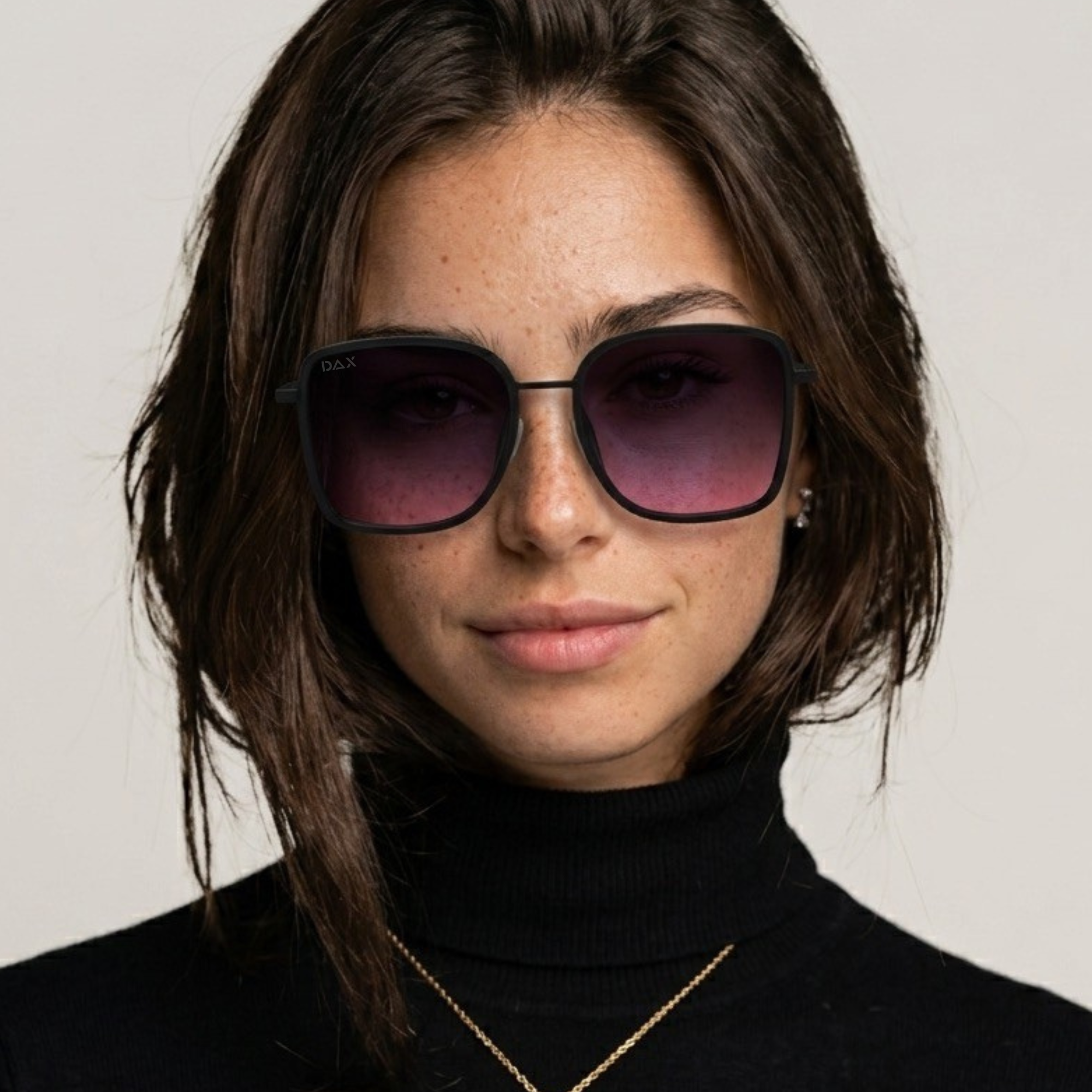 Woman wearing dark sunglasses and a black turtleneck against a neutral background