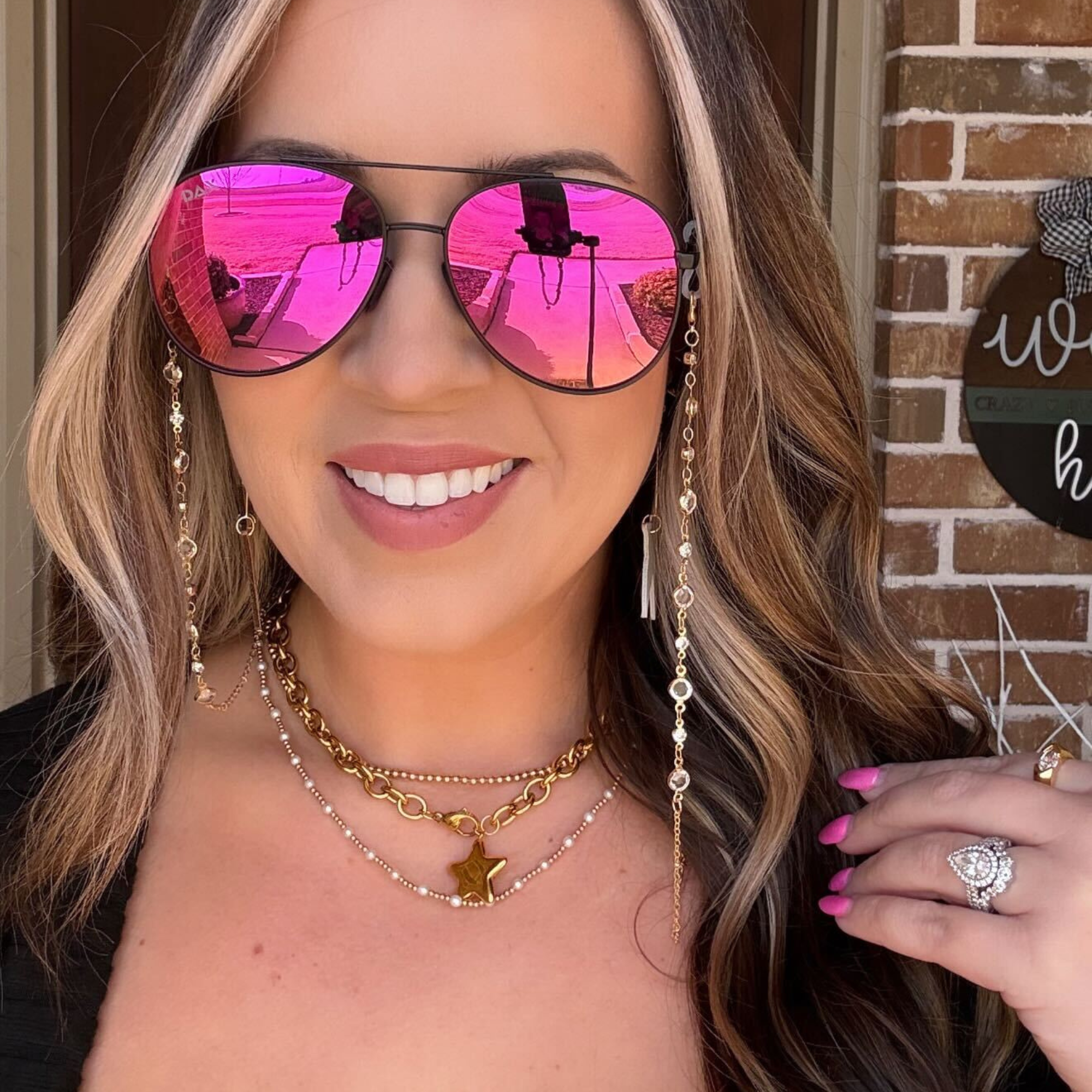 Woman wearing pink reflective sunglasses with a brick wall background