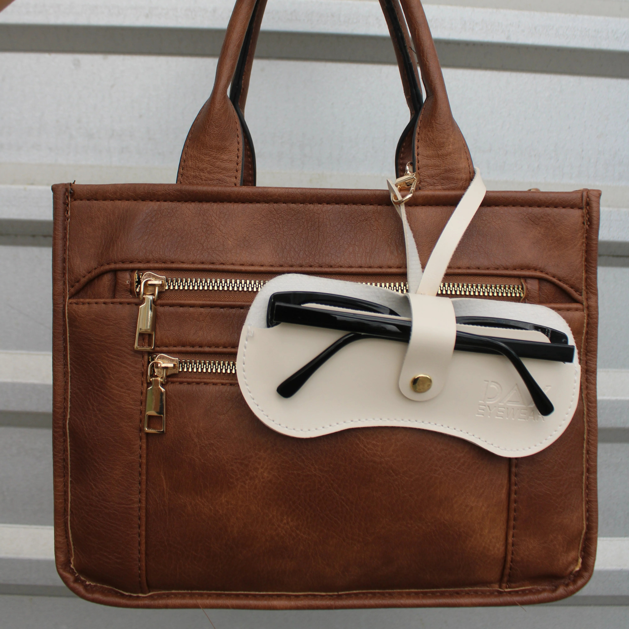 Brown leather handbag with a white patch and gold zipper on a striped background
