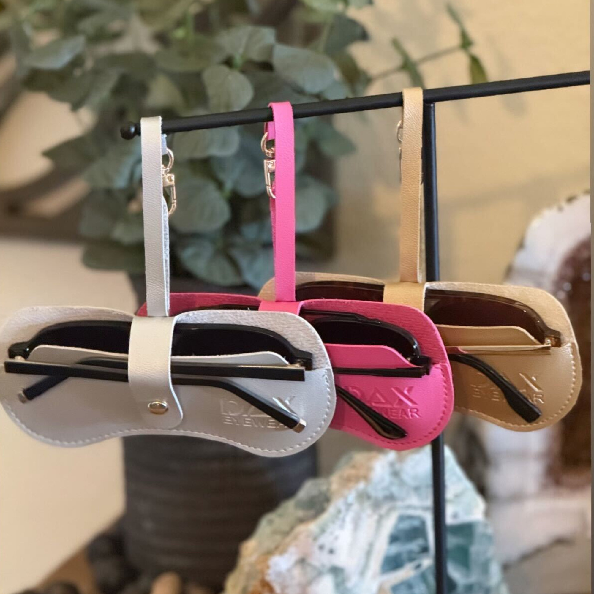 Three pairs of sunglasses in different cases hanging on a rack with a blurred background.