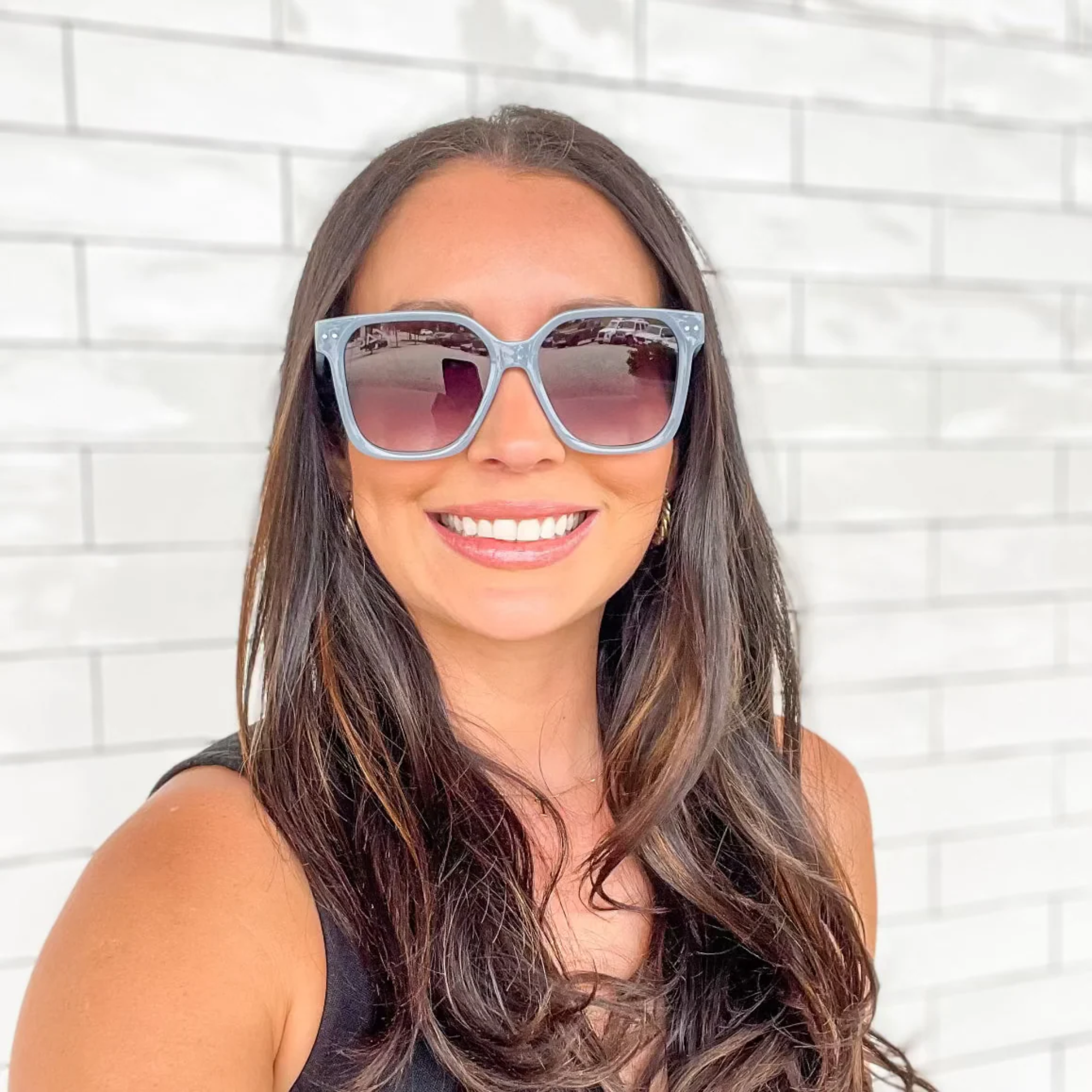 Woman wearing sunglasses with a white brick wall background