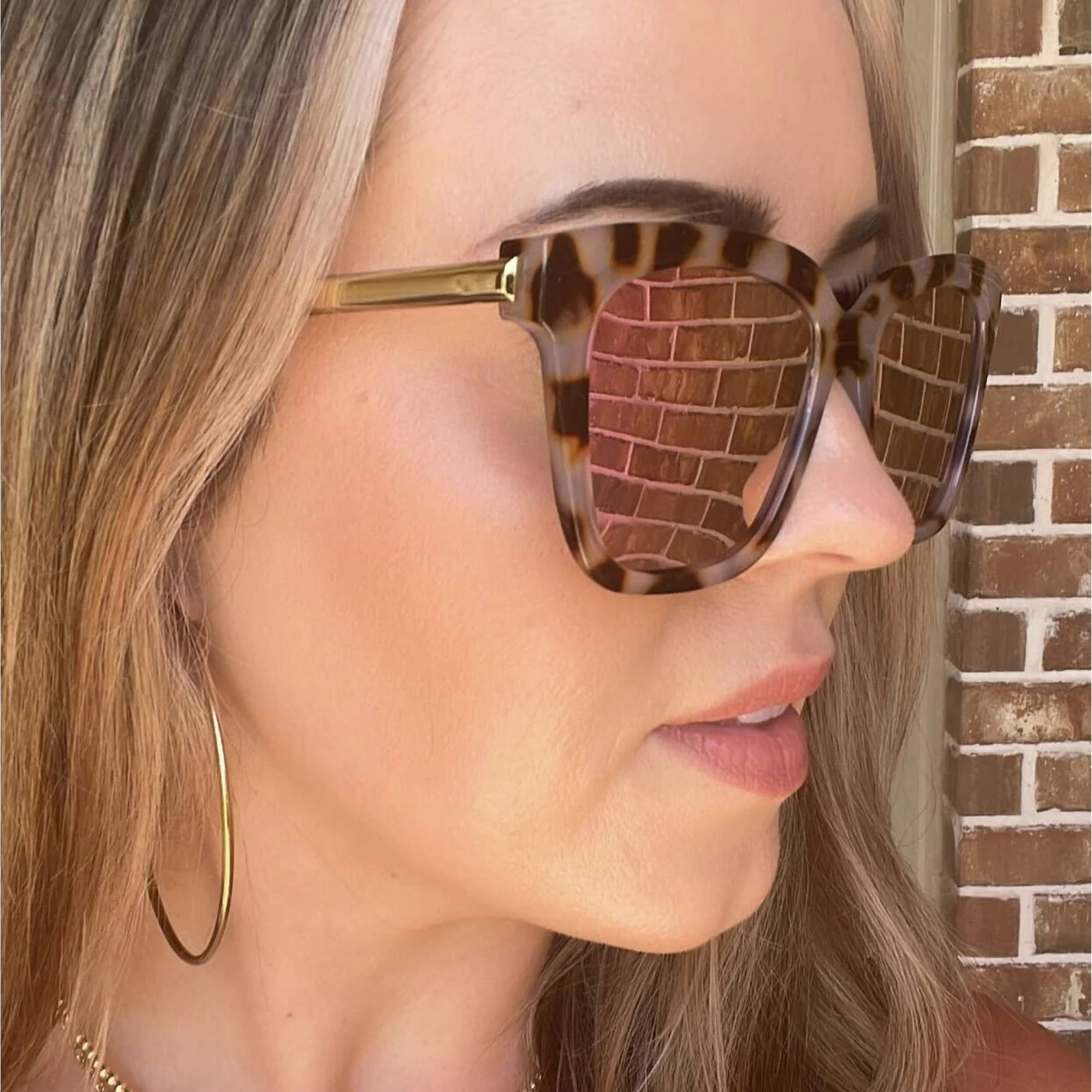 Close-up of a person wearing tortoiseshell sunglasses with a brick wall background
