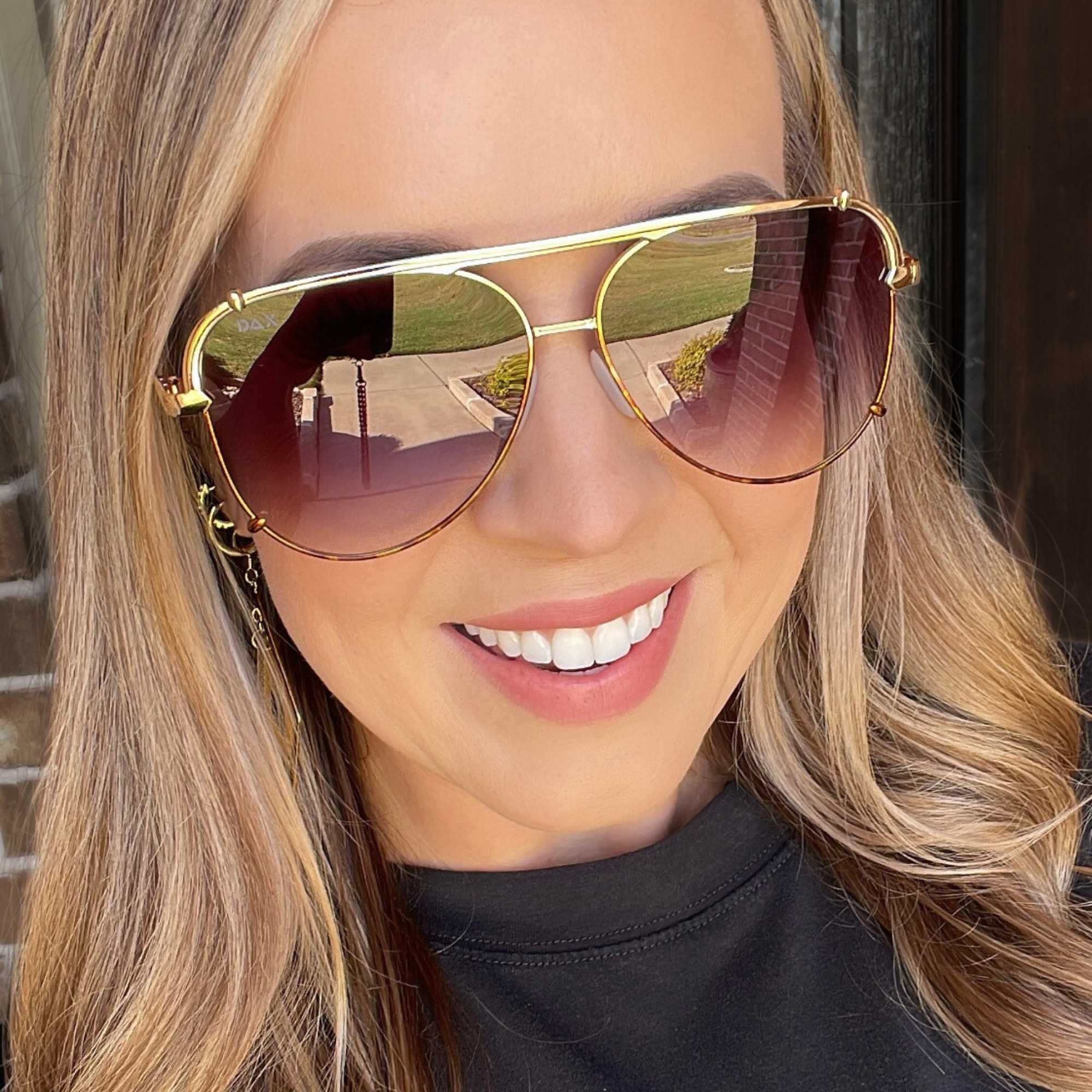 Close-up of a person wearing gold-framed sunglasses with a blurred background