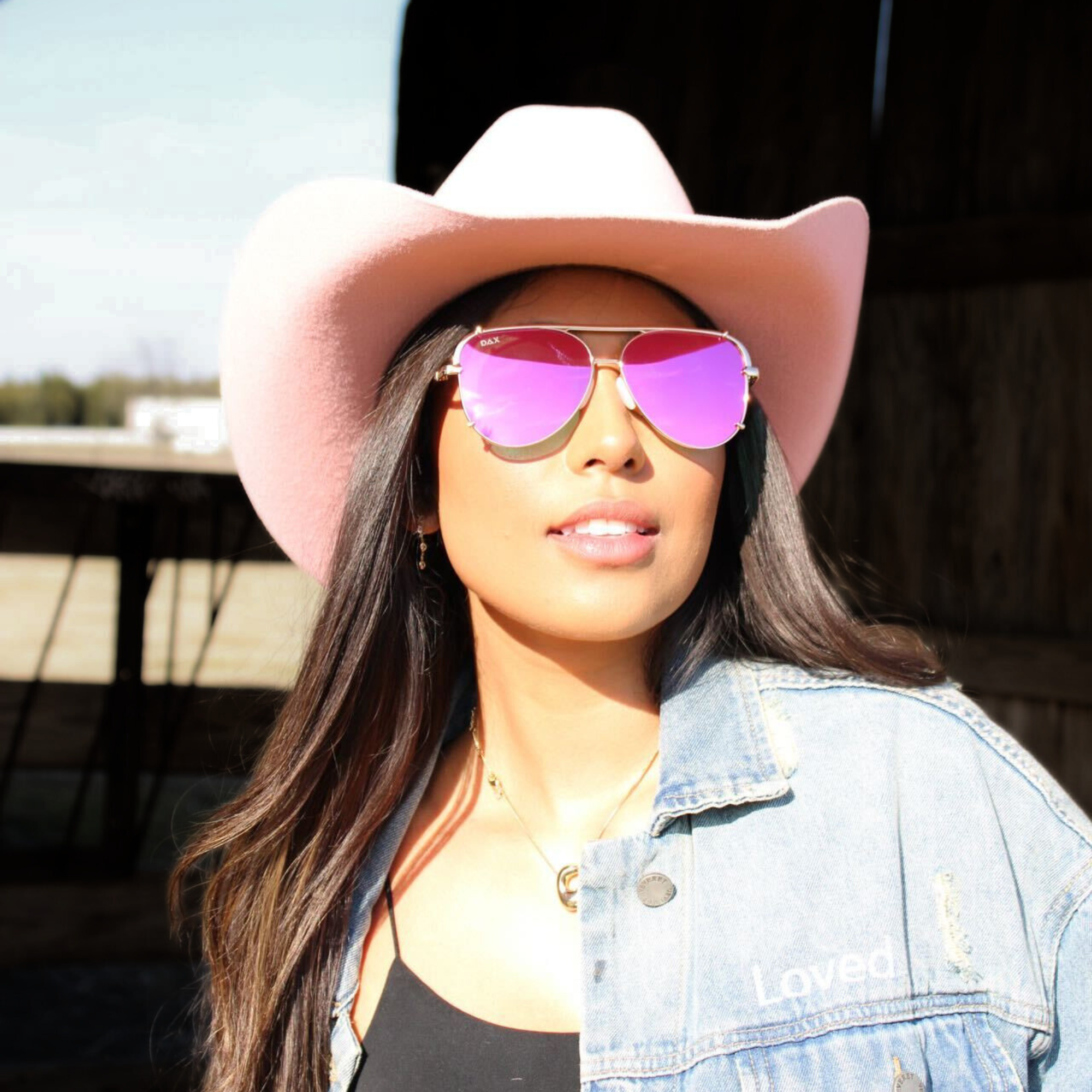 Woman wearing a pink cowboy hat and pink sunglasses with a blurred background