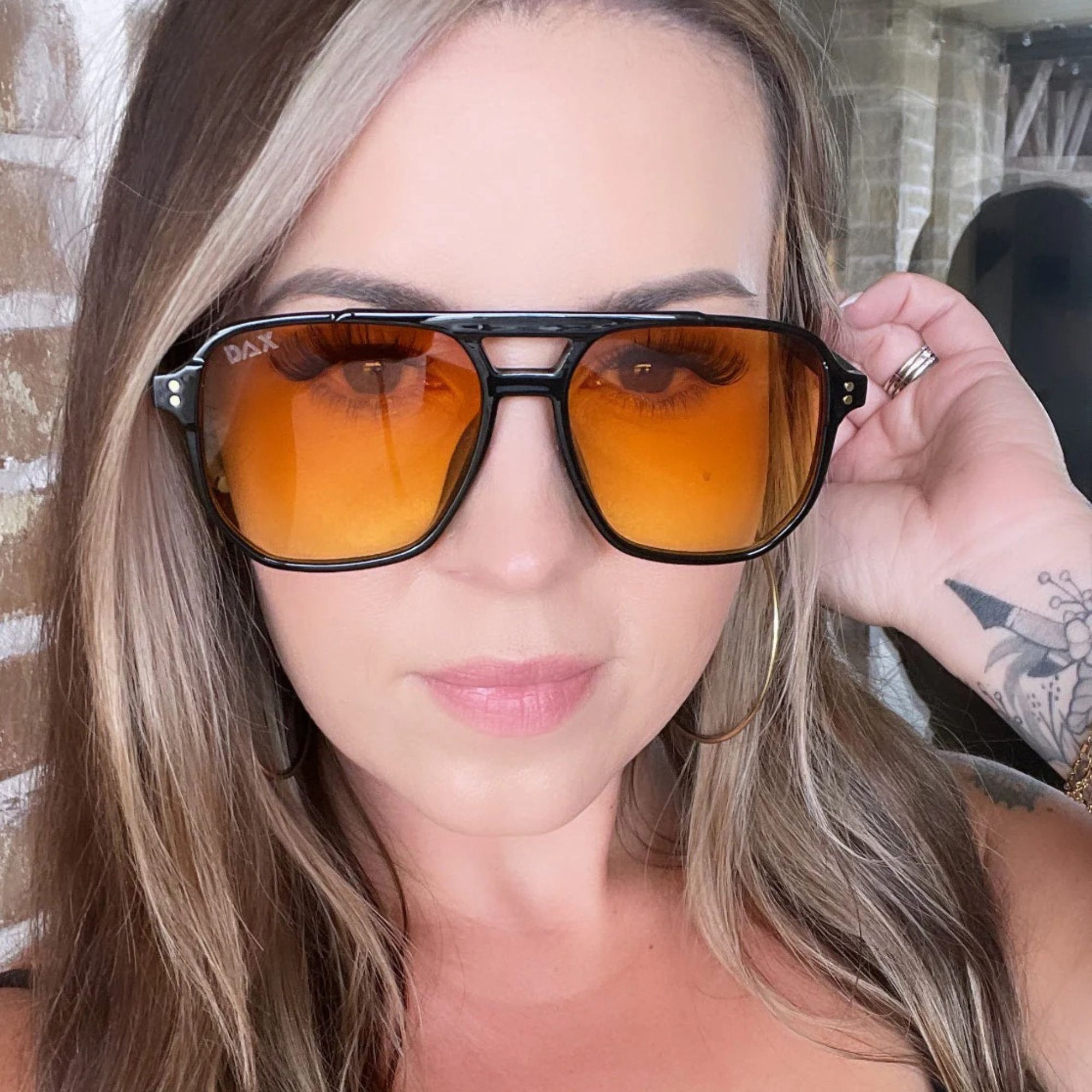 Woman wearing orange-tinted sunglasses with a blurred background