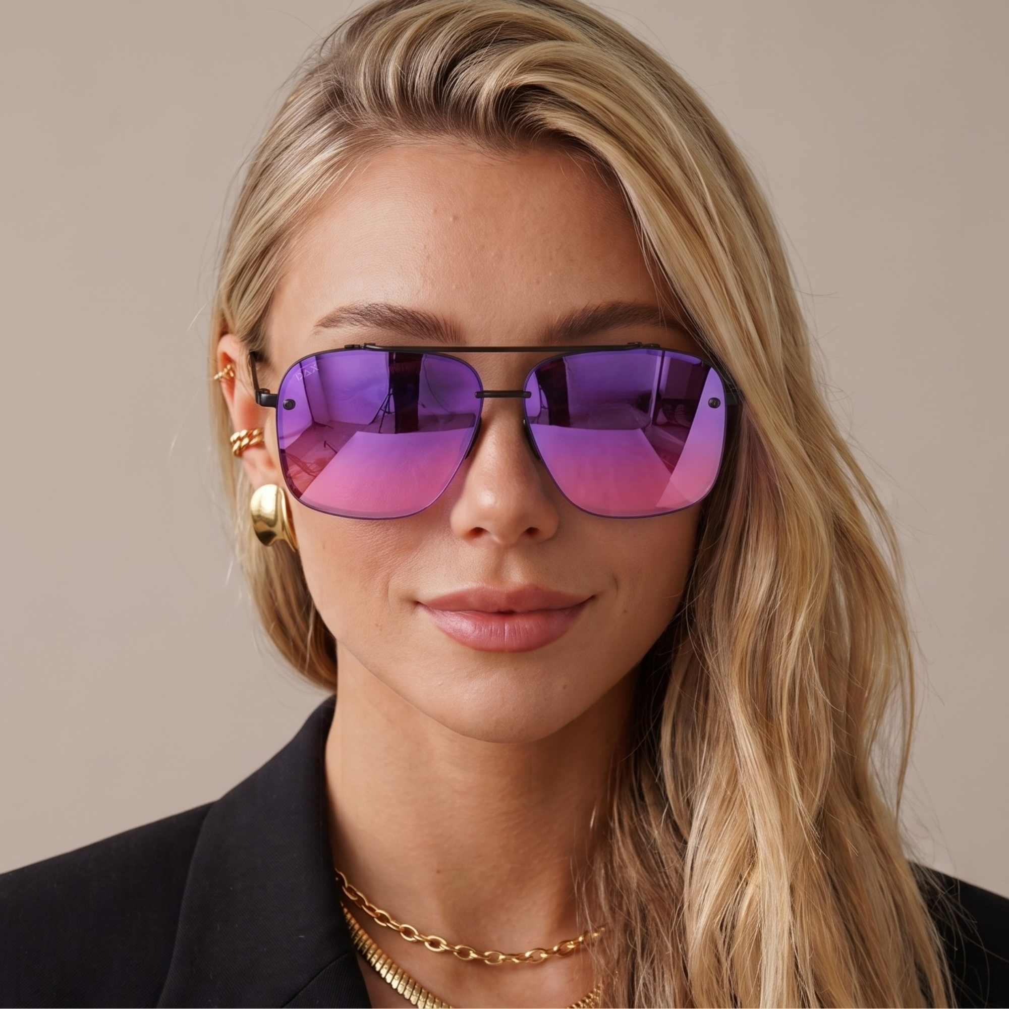 A close-up of a woman with blonde hair wearing aviator-style sunglasses with a black frame and vibrant purple-to-pink mirrored lenses, accessorized with gold earrings and necklaces.