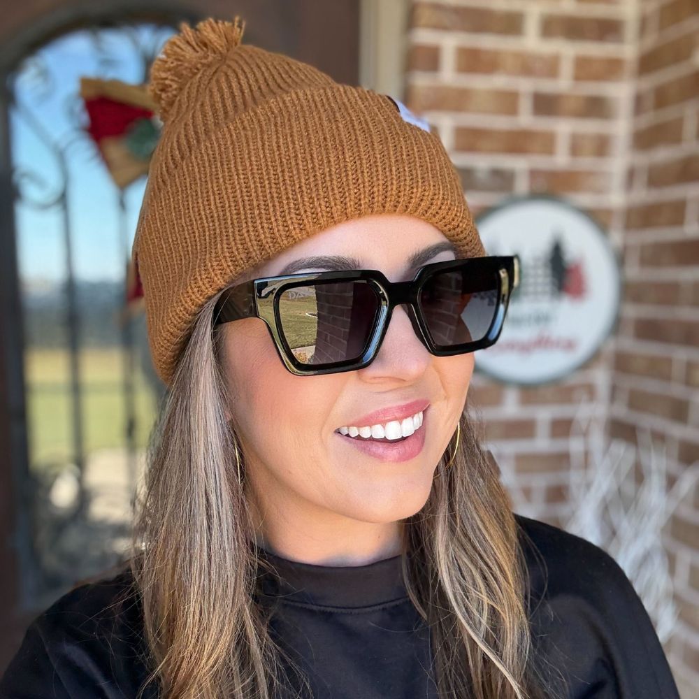 Person wearing a brown knit beanie and sunglasses with a brick building in the background