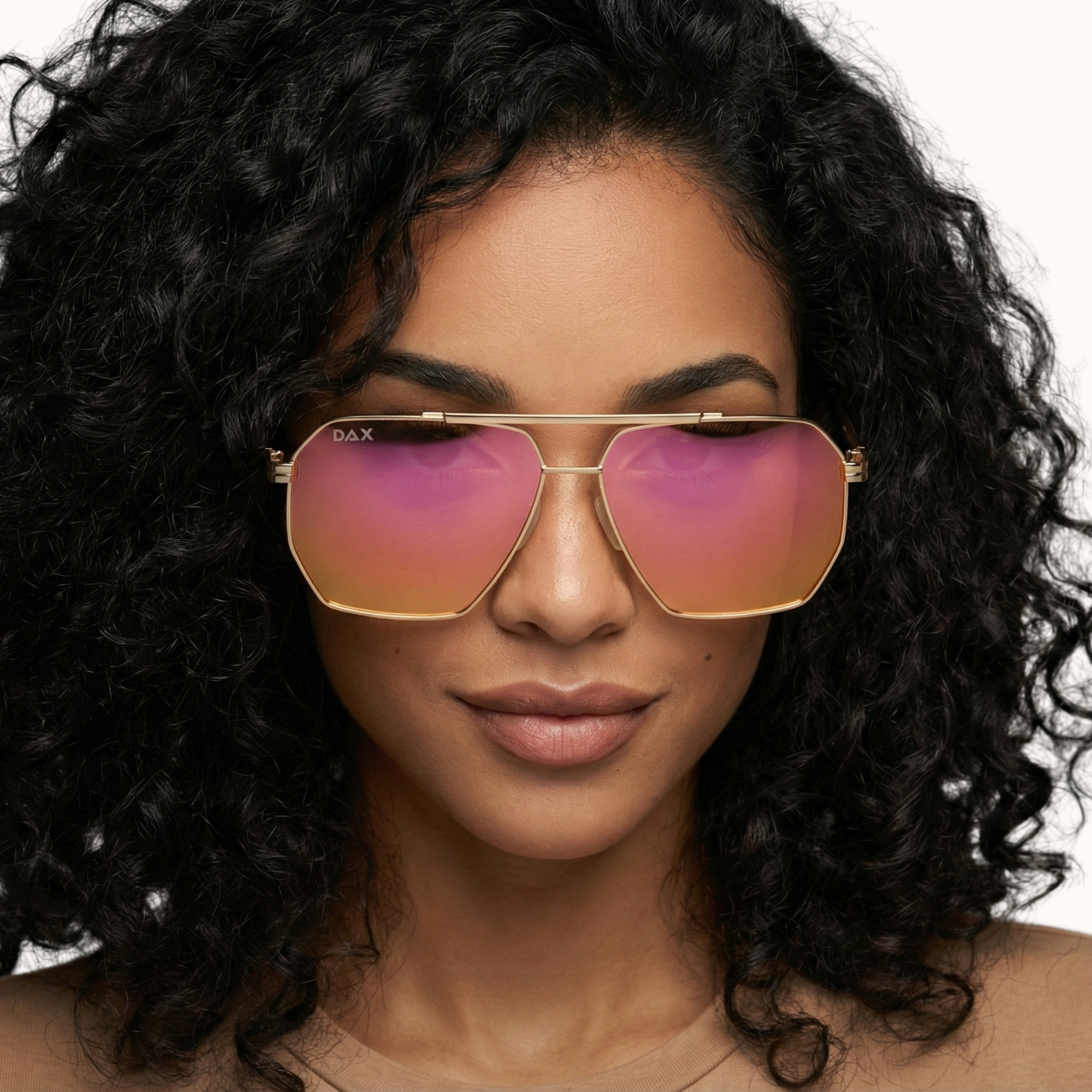 Woman wearing gold-framed sunglasses with pink lenses on a neutral background