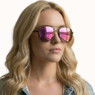 Woman wearing pink reflective sunglasses with a plain background