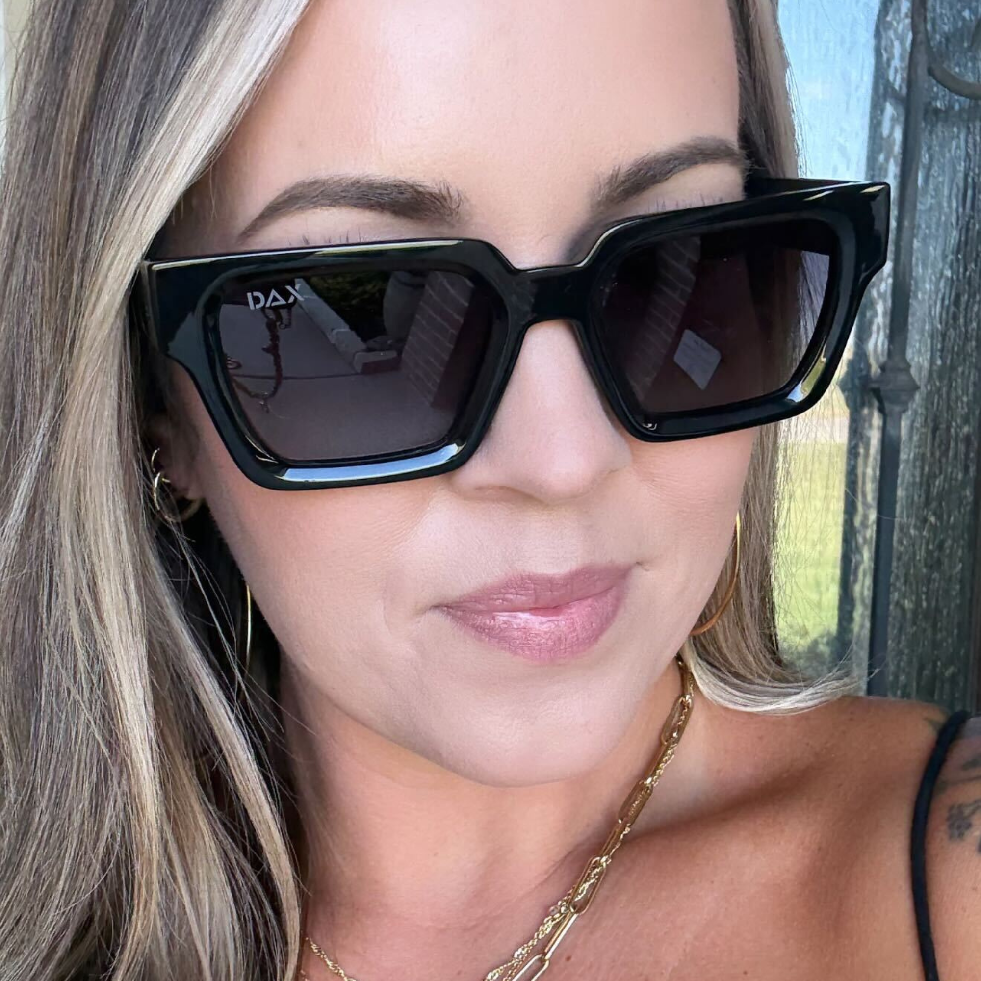 Close-up of a person wearing black sunglasses with 'DAX' branding.