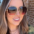 Woman wearing gold-framed sunglasses with a brick wall background