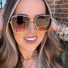Woman wearing gold-framed sunglasses with a brick wall background