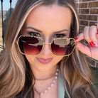 Woman holding up a pair of sunglasses with a brick wall background