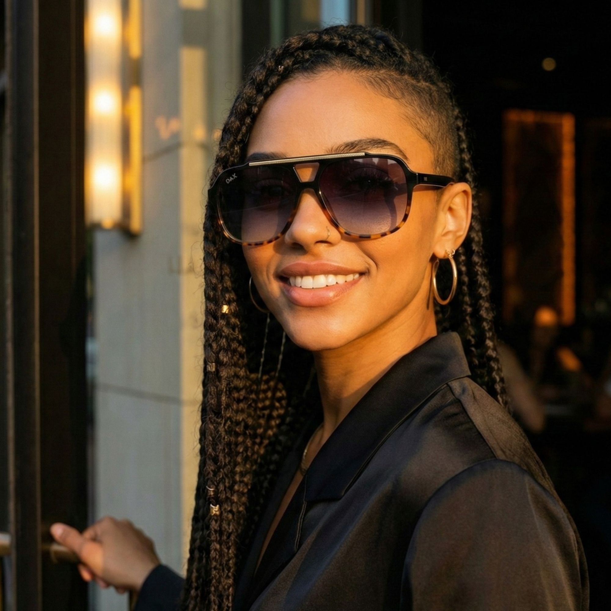 Woman wearing sunglasses and a black outfit, standing outdoors with blurred background