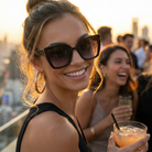 Woman wearing sunglasses and holding a drink with a blurred background of people and cityscape.