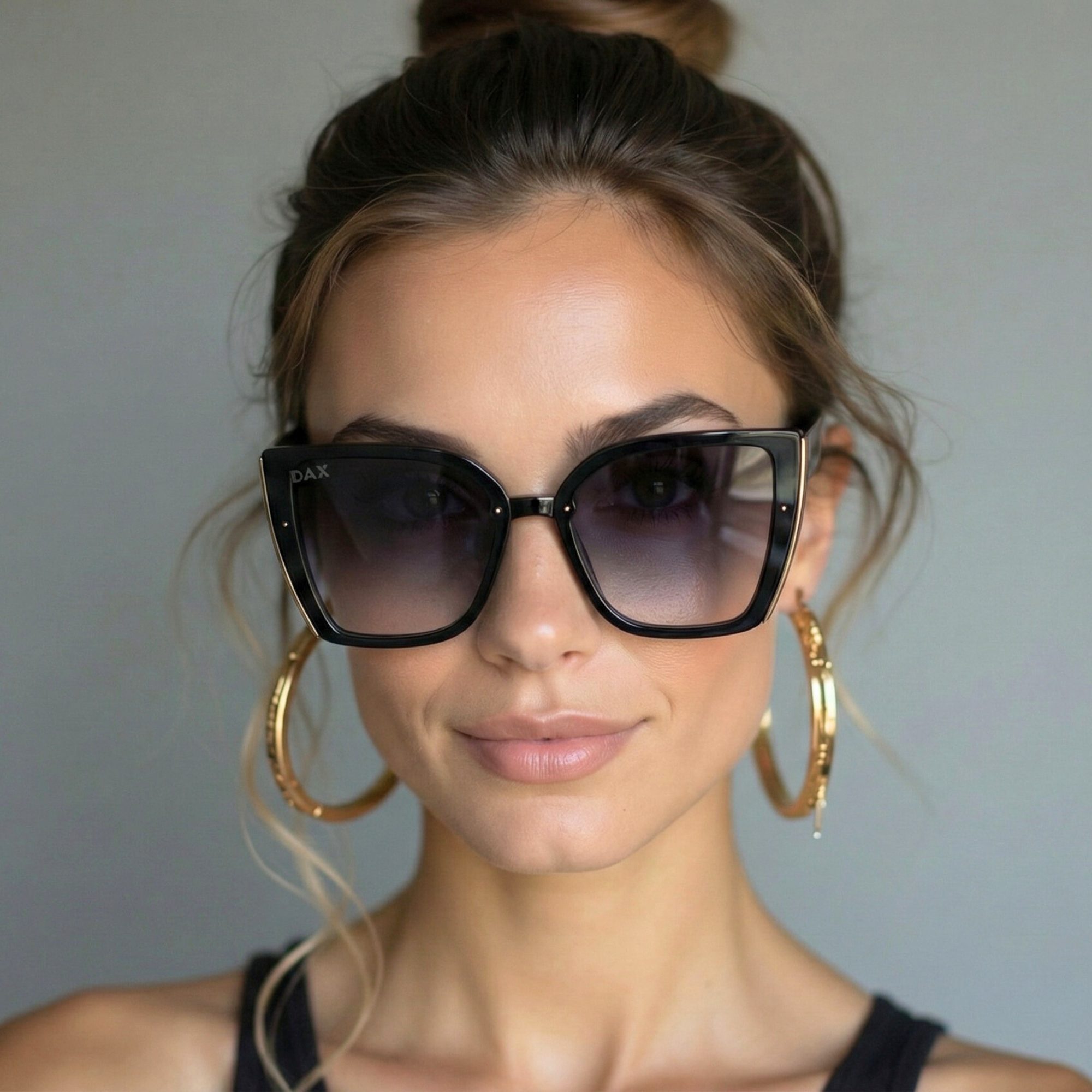 Woman wearing large black sunglasses and gold hoop earrings against a neutral background