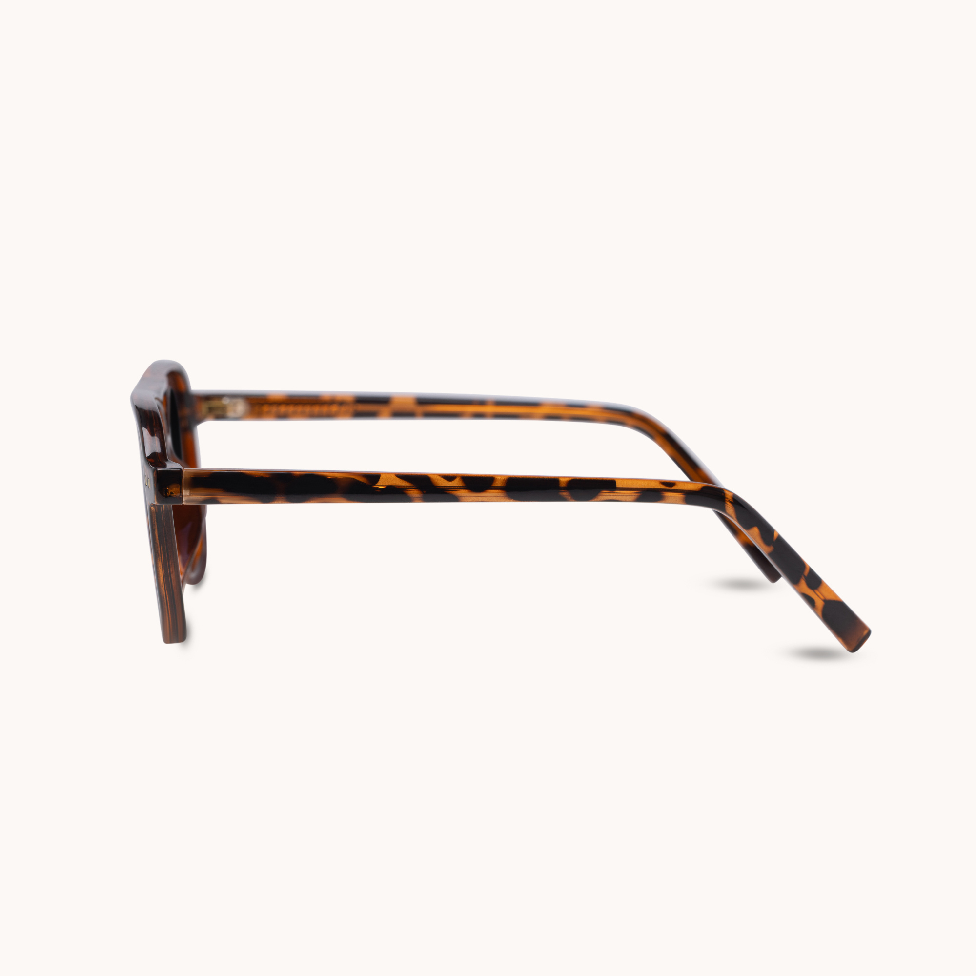 A pair of square-frame eyeglasses with a classic tortoiseshell pattern in brown and amber, shown from a side profile view against a light cream background.