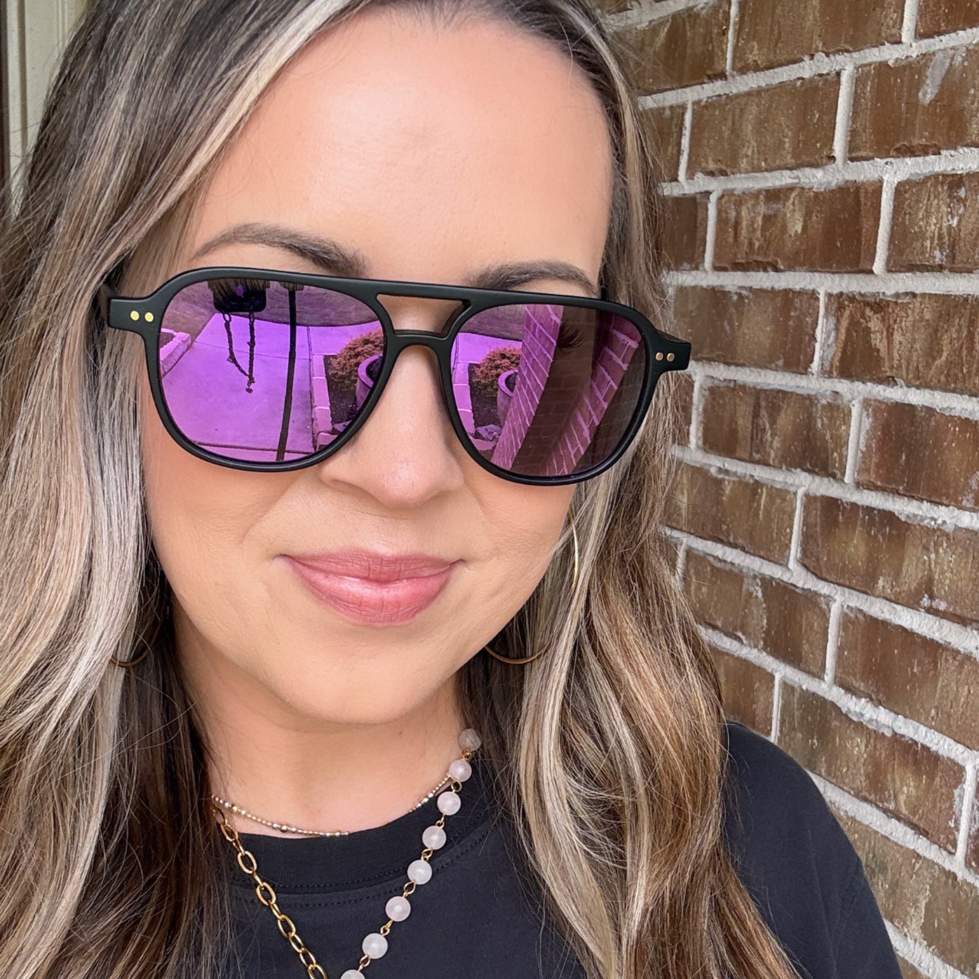 Woman wearing purple reflective sunglasses in front of a brick wall