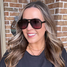 Woman wearing sunglasses and hoop earrings in front of a brick wall