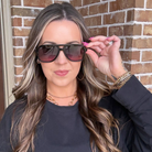 Woman wearing sunglasses and a black jacket in front of a brick wall
