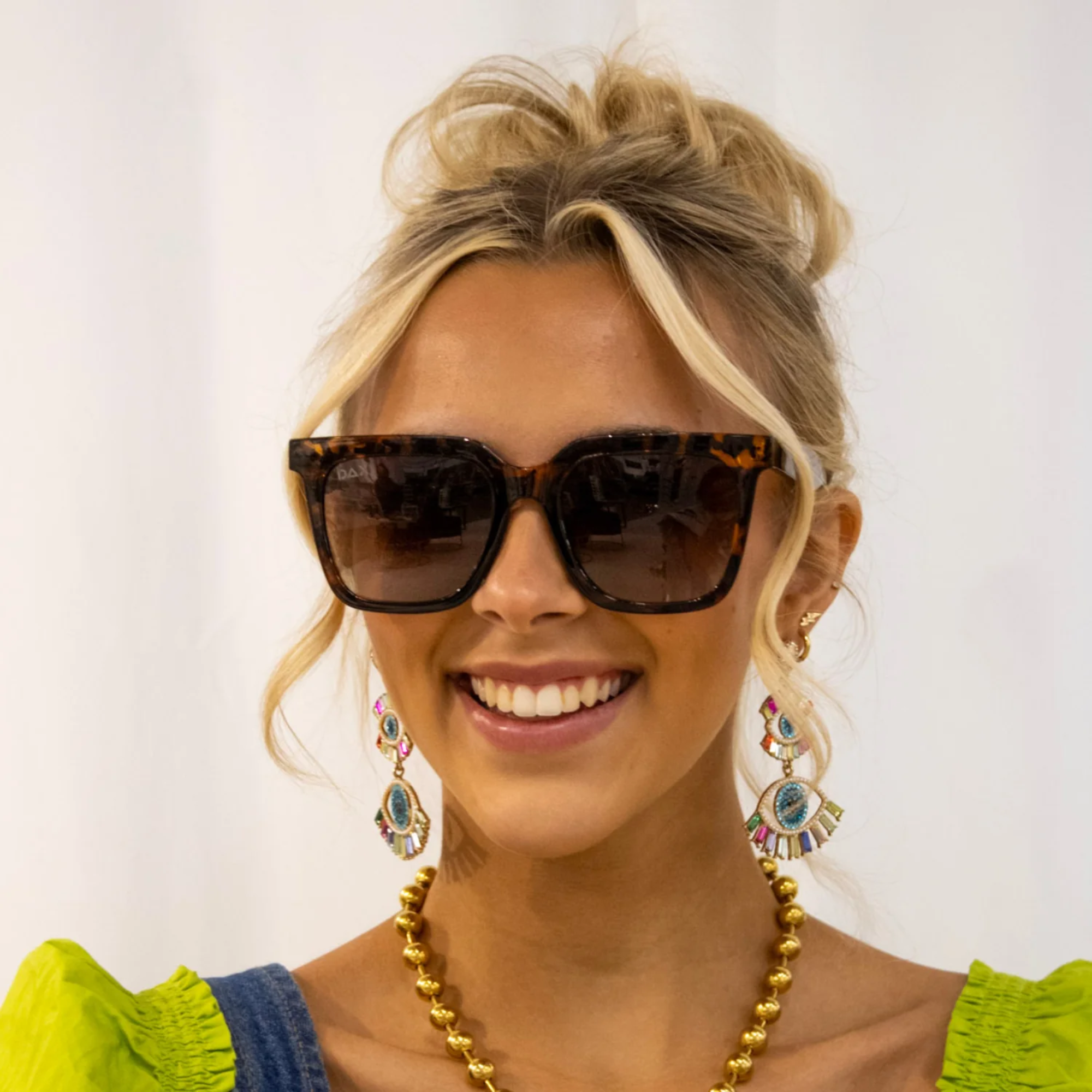 Woman wearing sunglasses and colorful earrings with a plain background
