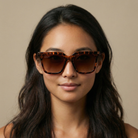 Woman wearing cheetah sunglasses with a neutral background