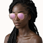 Woman wearing gold-framed sunglasses with pink lenses on a white background