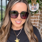 Woman wearing sunglasses with a 'Home Sweet Home' sign in the background