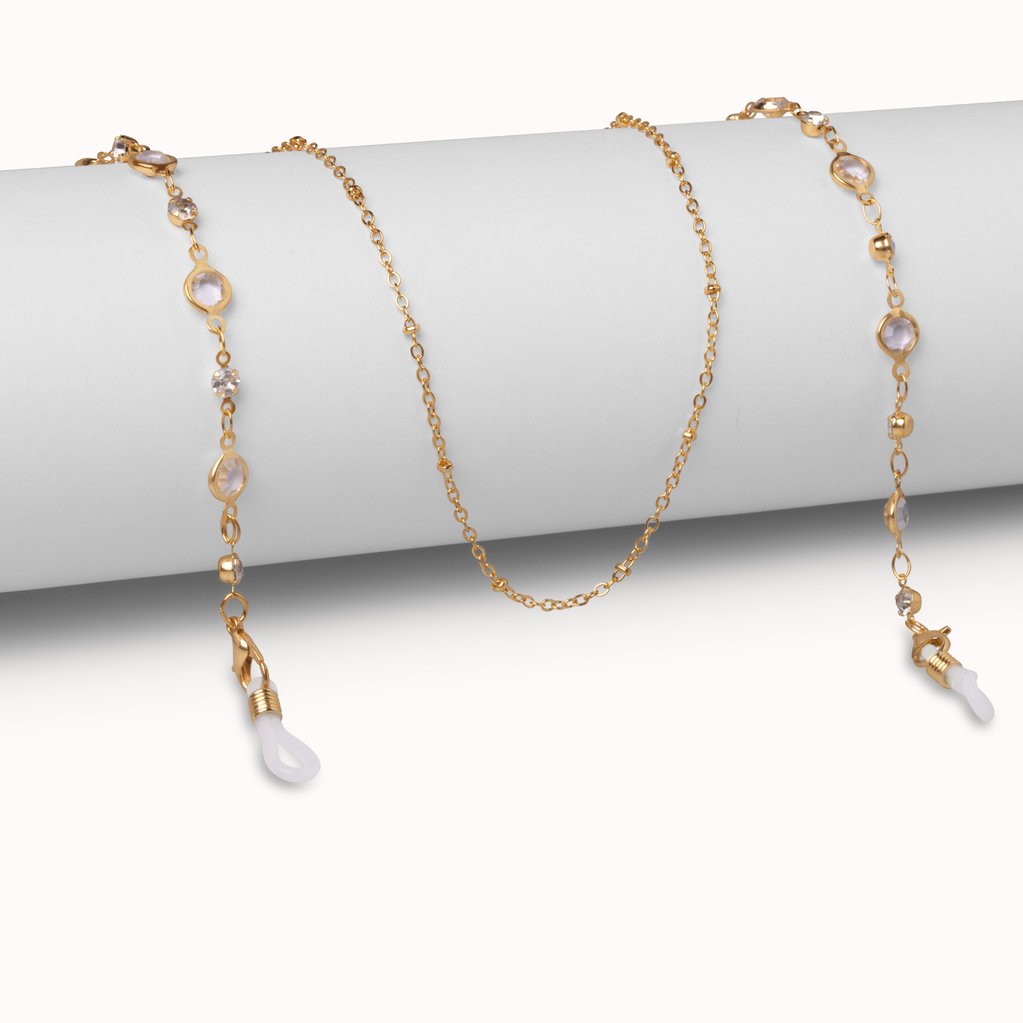 A delicate gold chain necklace draped over a white cylindrical display stand, featuring small gold beads, clear faceted stones, and white teardrop-shaped pendant drops.
