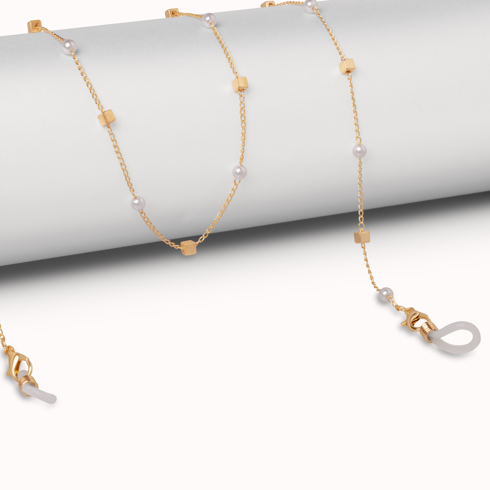 A delicate gold chain necklace with small gold cube beads and white pearl-like beads, draped over a light gray cylindrical display stand on a white background.