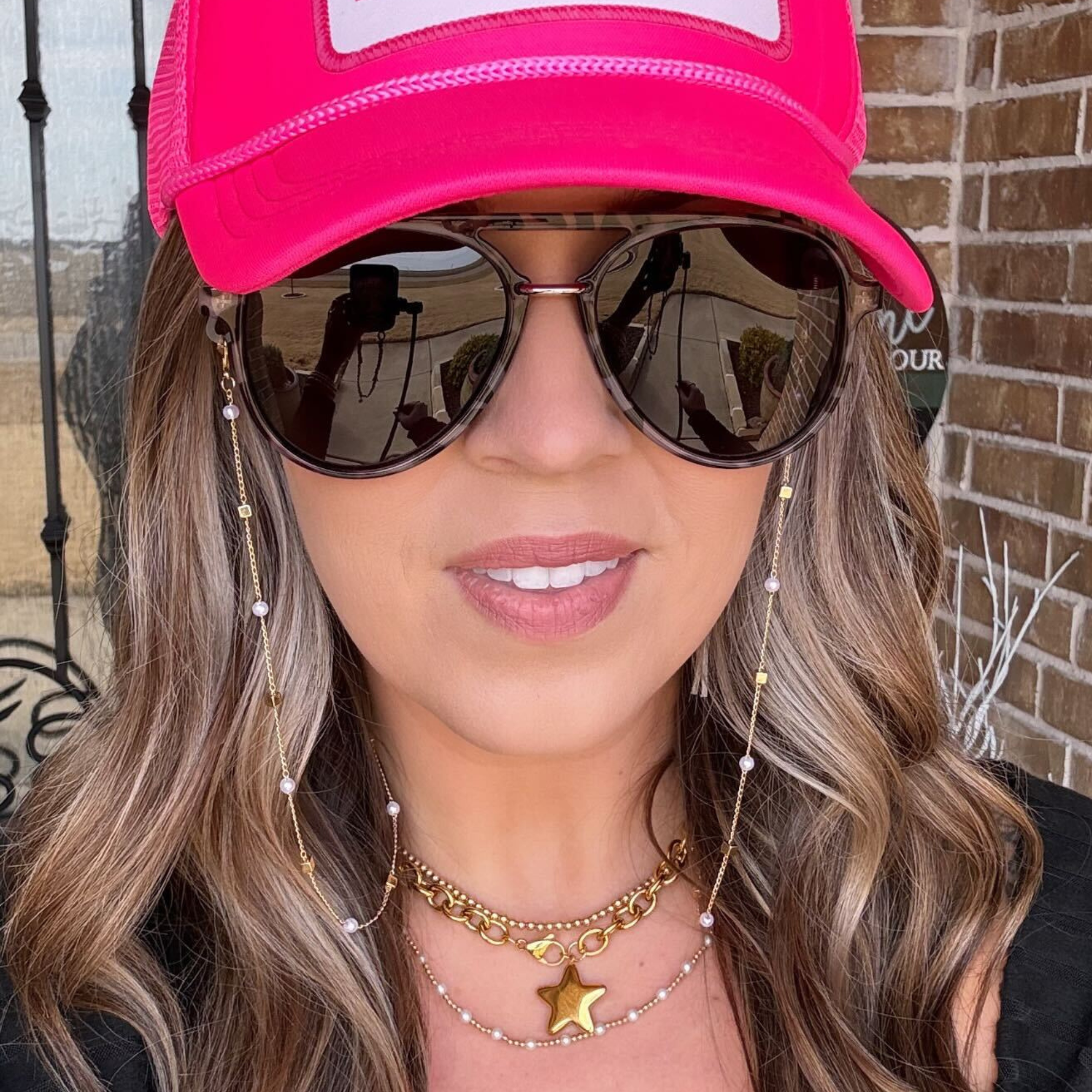 Woman wearing a pink cap and sunglasses with a brick wall background