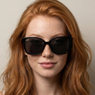 Woman wearing large black sunglasses with a neutral background
