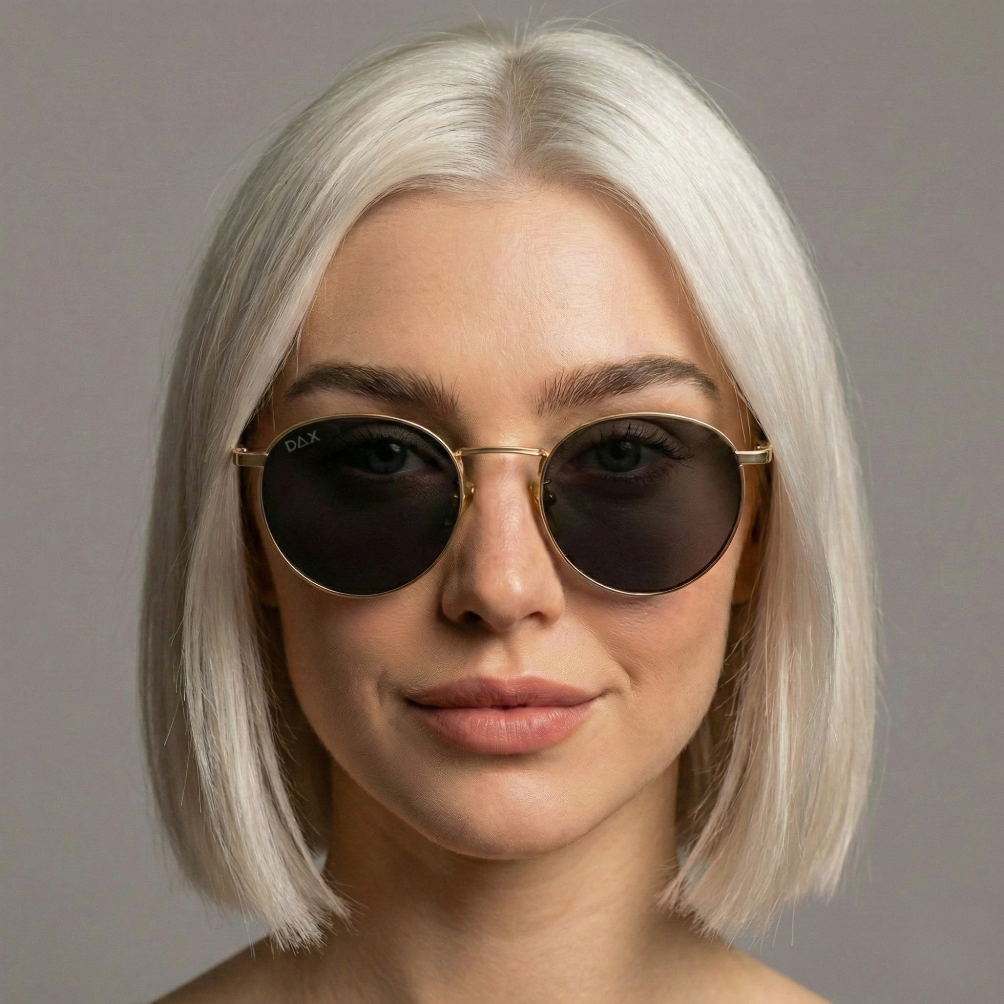 Person with platinum blonde hair wearing dark sunglasses against a gray background