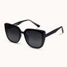 Black cat-eye sunglasses with dark gradient lenses, shown at an angle on a light cream background.