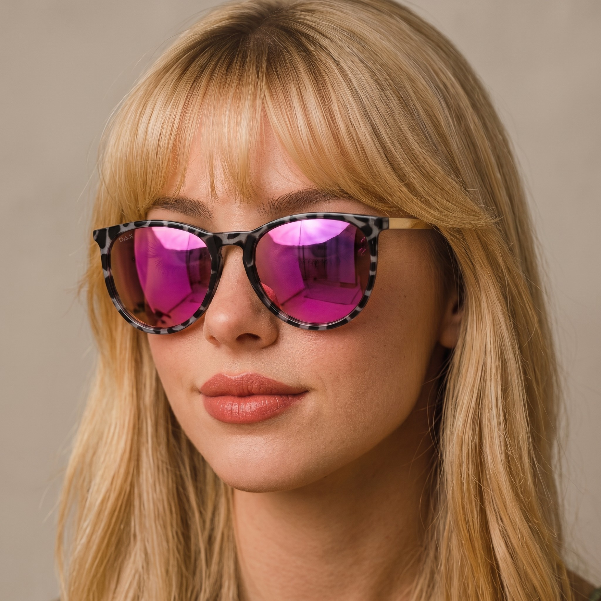 A close-up of a woman with blonde hair wearing oversized sunglasses with a tortoiseshell patterned frame and vibrant pink mirrored lenses.
