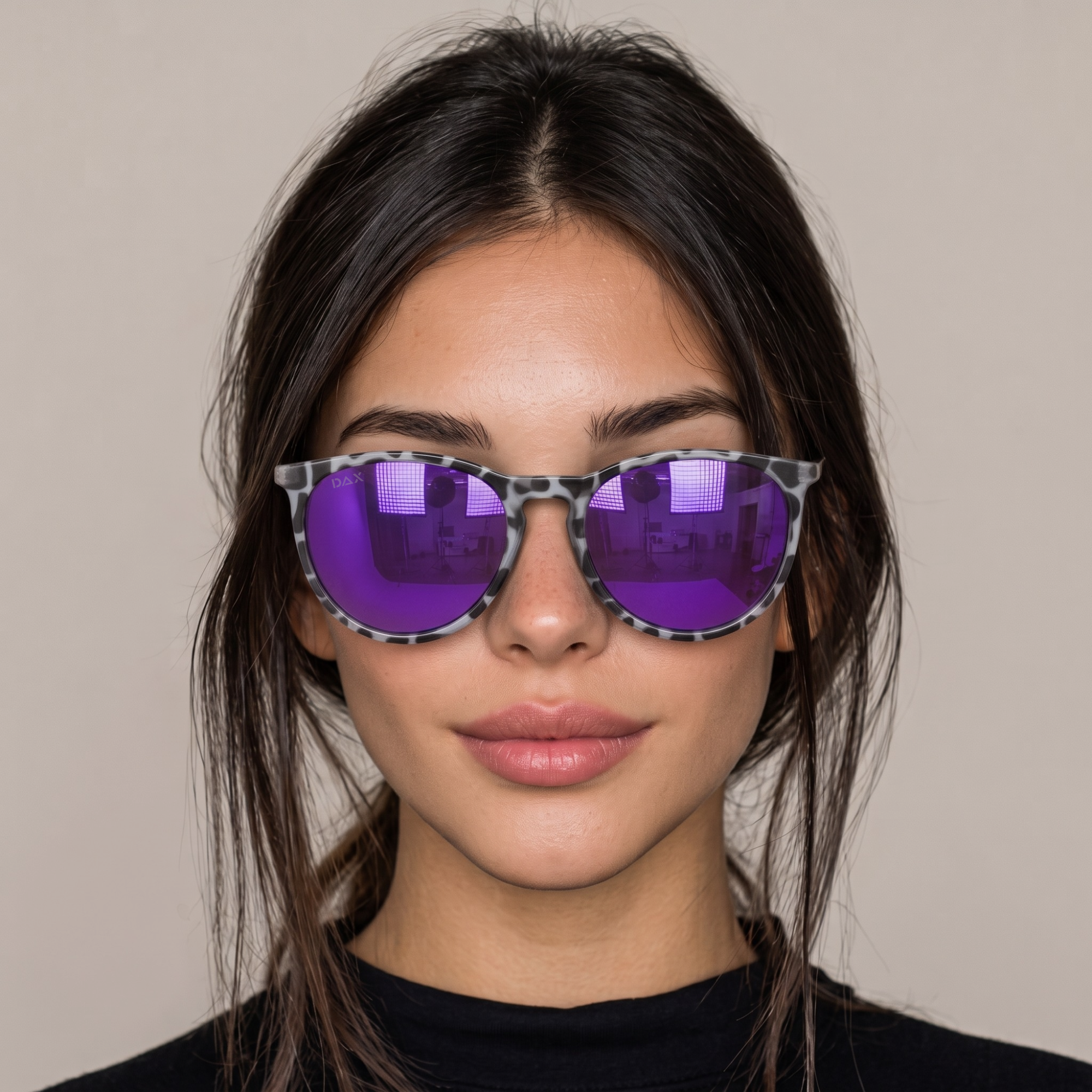 A close-up of a woman wearing round sunglasses with a gray and black tortoiseshell patterned frame and vibrant purple mirrored lenses, set against a plain beige background.